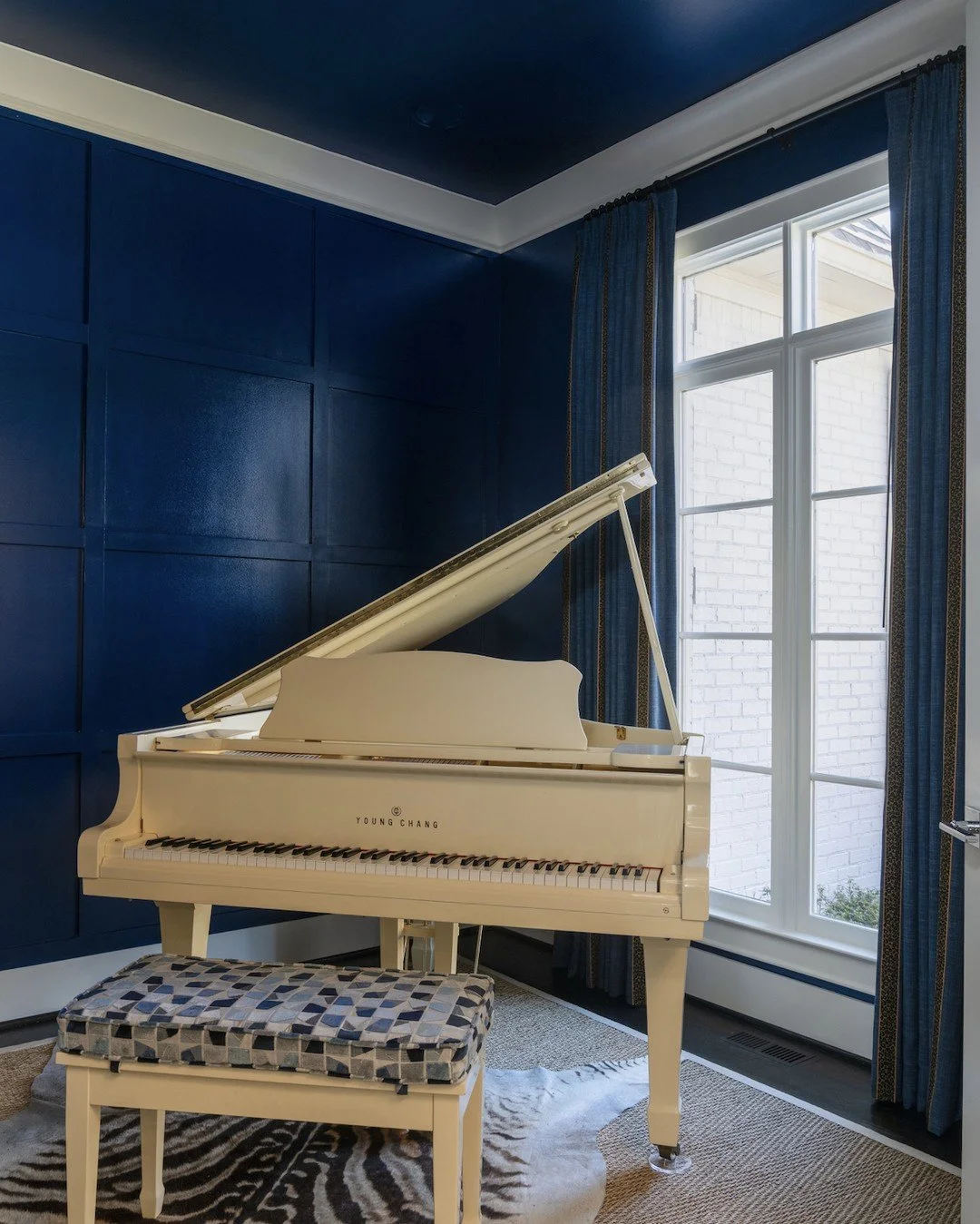 This one was a hard sell, but it was so worth it. Lacquered walls in a deep blue set the stage, and custom drapery with olive and leopard trim runs the length of the panels in three sections. A geometric raised velvet cushion on the piano bench makes