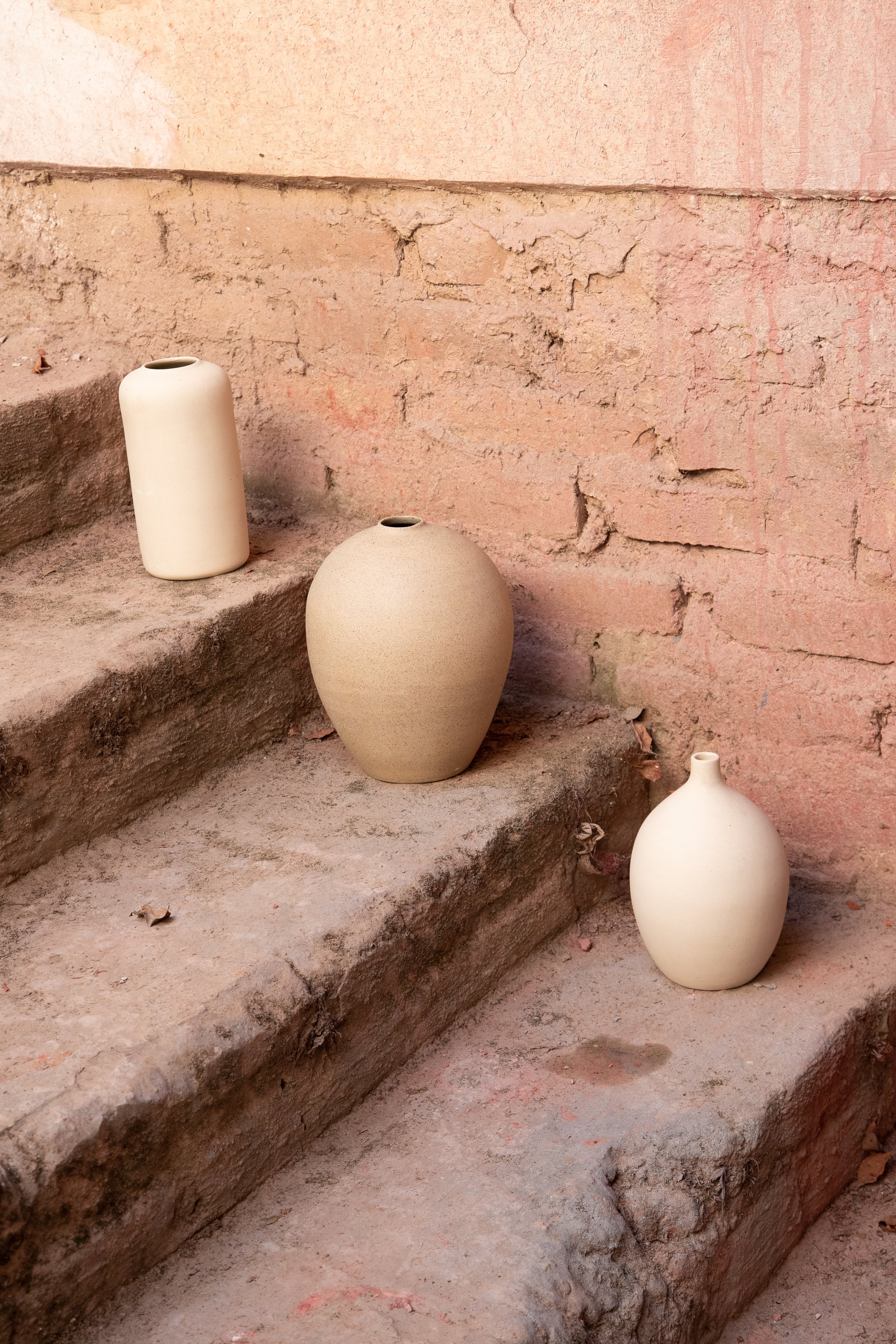 Three clay vases on stone steps with a rustic, textured wall in the background.