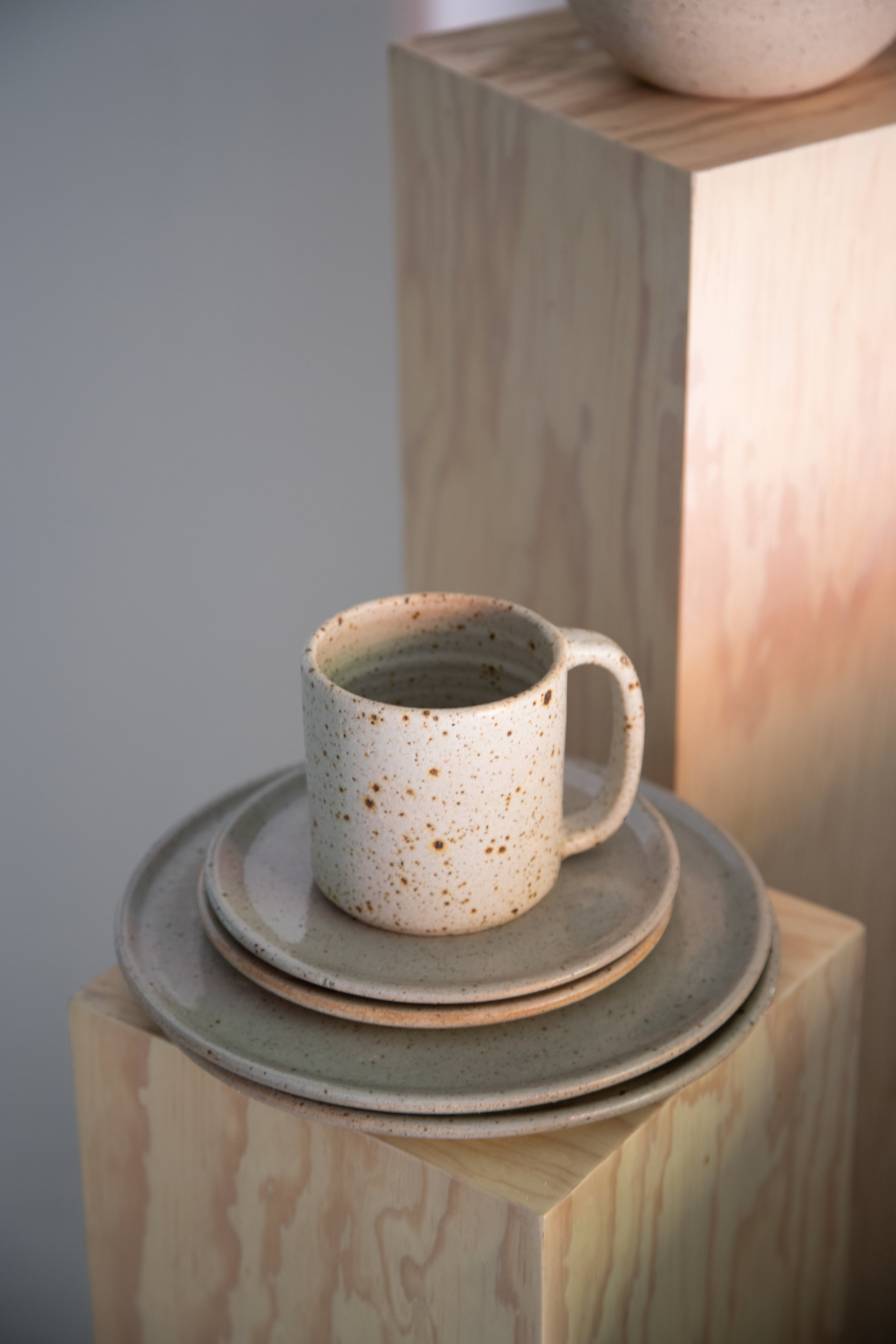 Ceramic speckled mug with matching plates on a wooden pedestal.