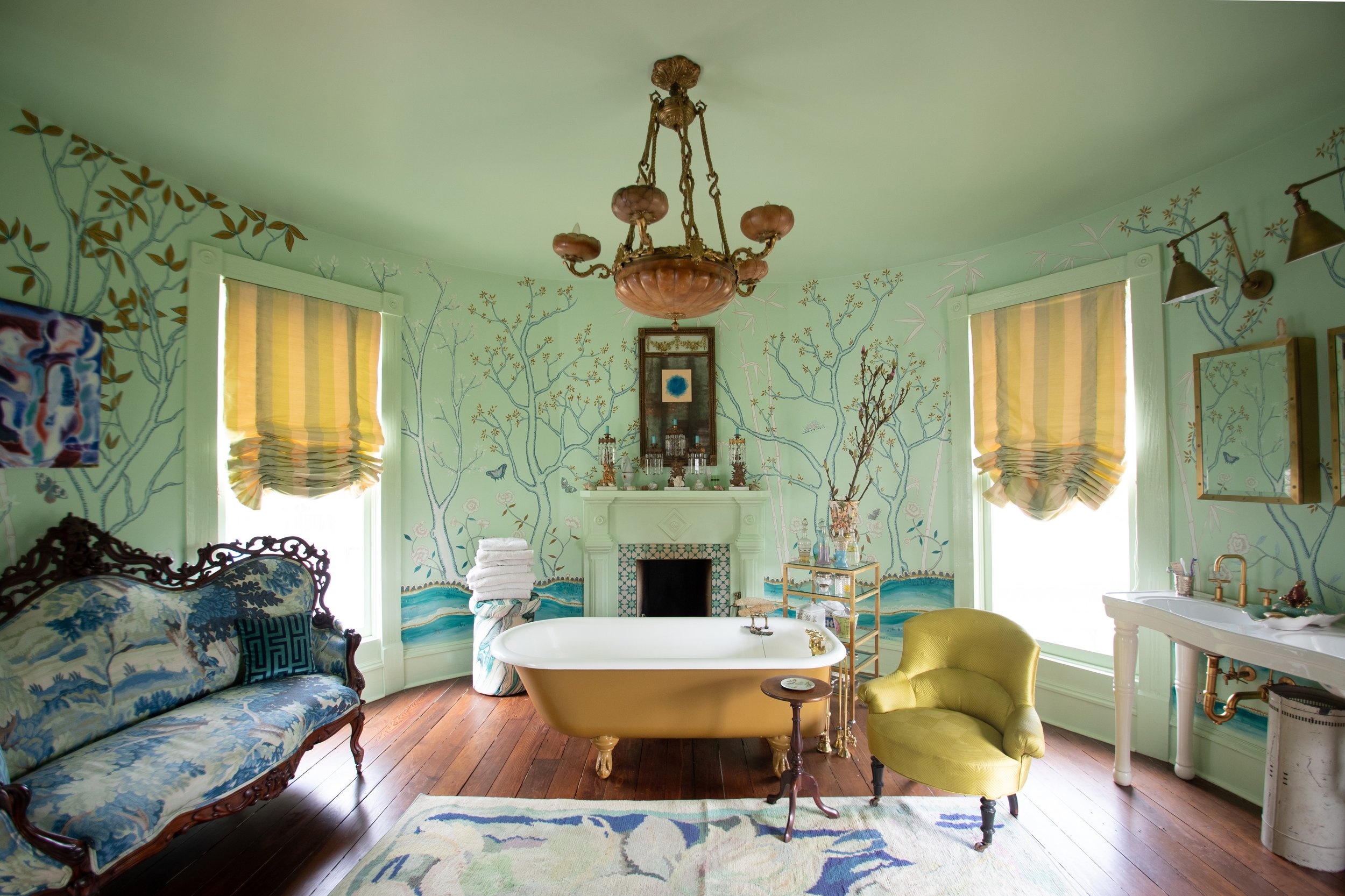 Luxurious bathroom with vintage furniture, floral wallpaper, clawfoot tub, ornate sofa, and chandelier.