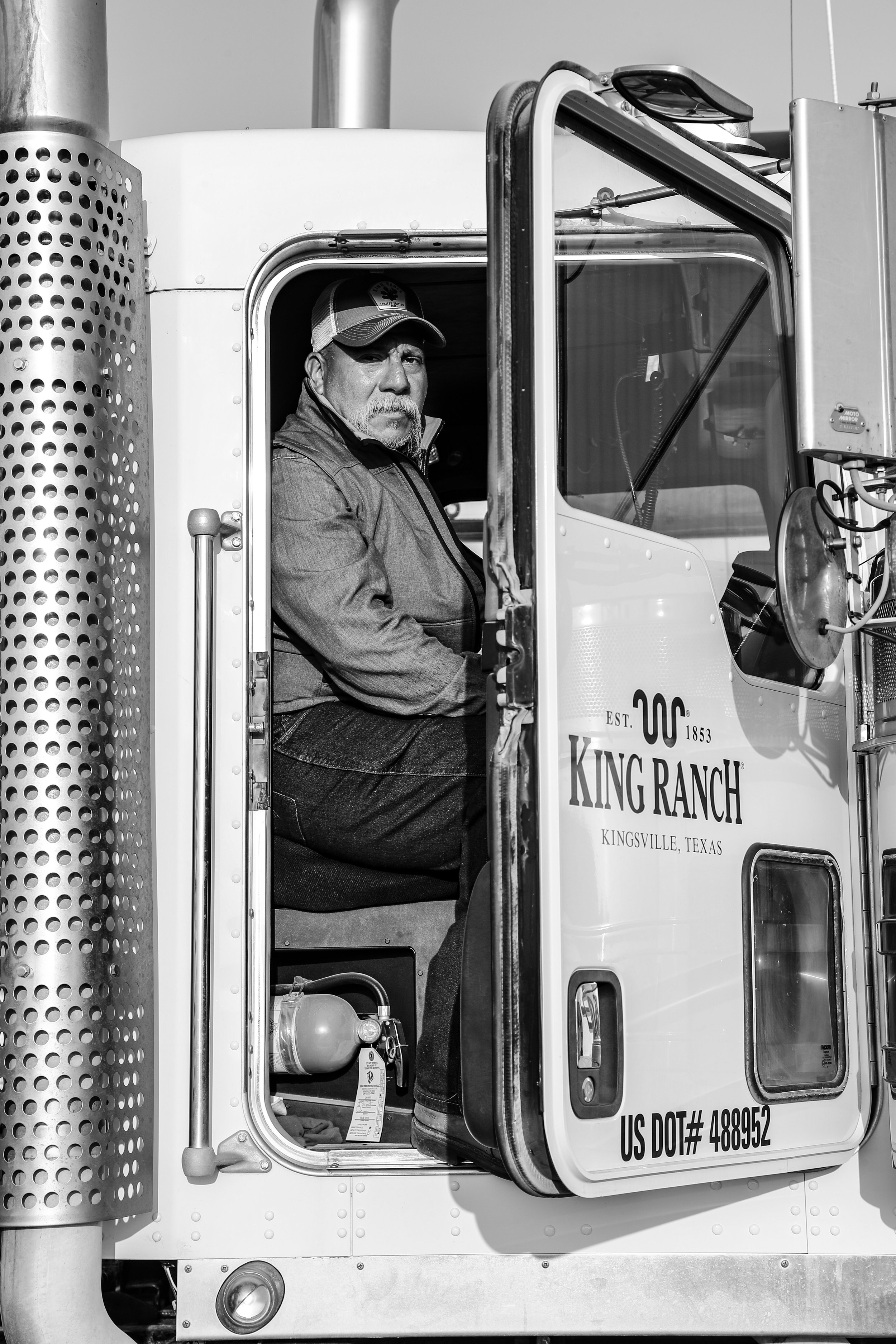 Man sitting in a truck cab, wearing a baseball cap, side door open, "King Ranch" logo visible.