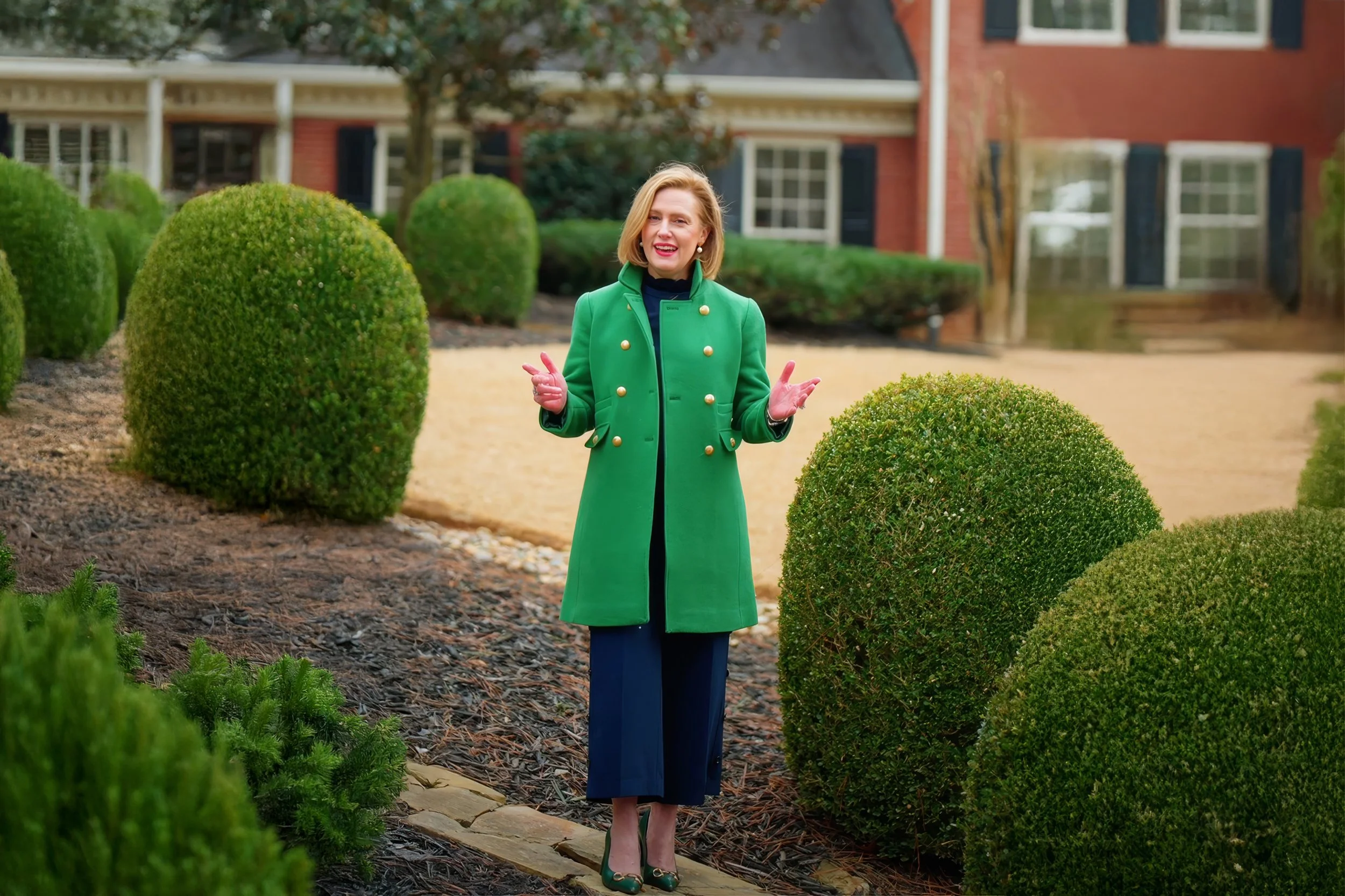 Smiling woman in blazer holding tablet outdoors with houses and plants in background