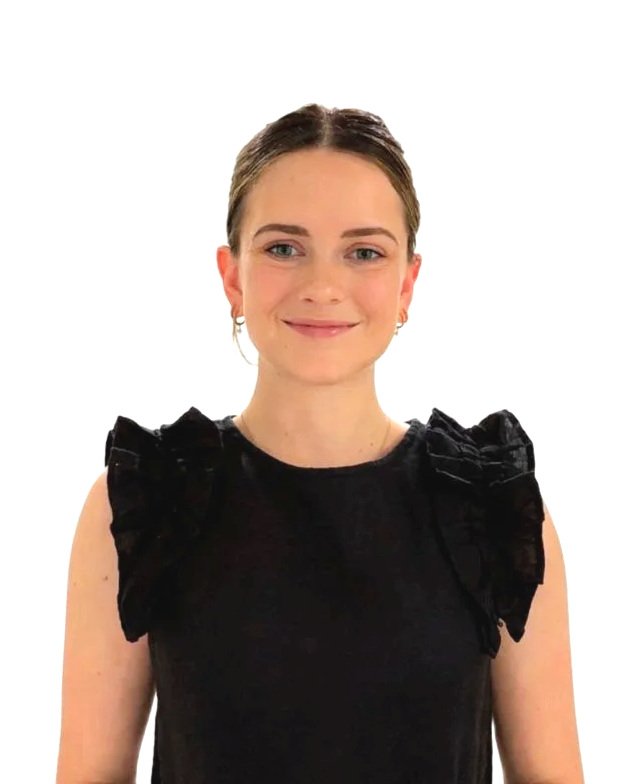 A young woman with fair skin and brown hair styled back, wearing a black sleeveless top with ruffle details on the shoulders, and small hoop earrings, smiling at the camera against a plain white background.