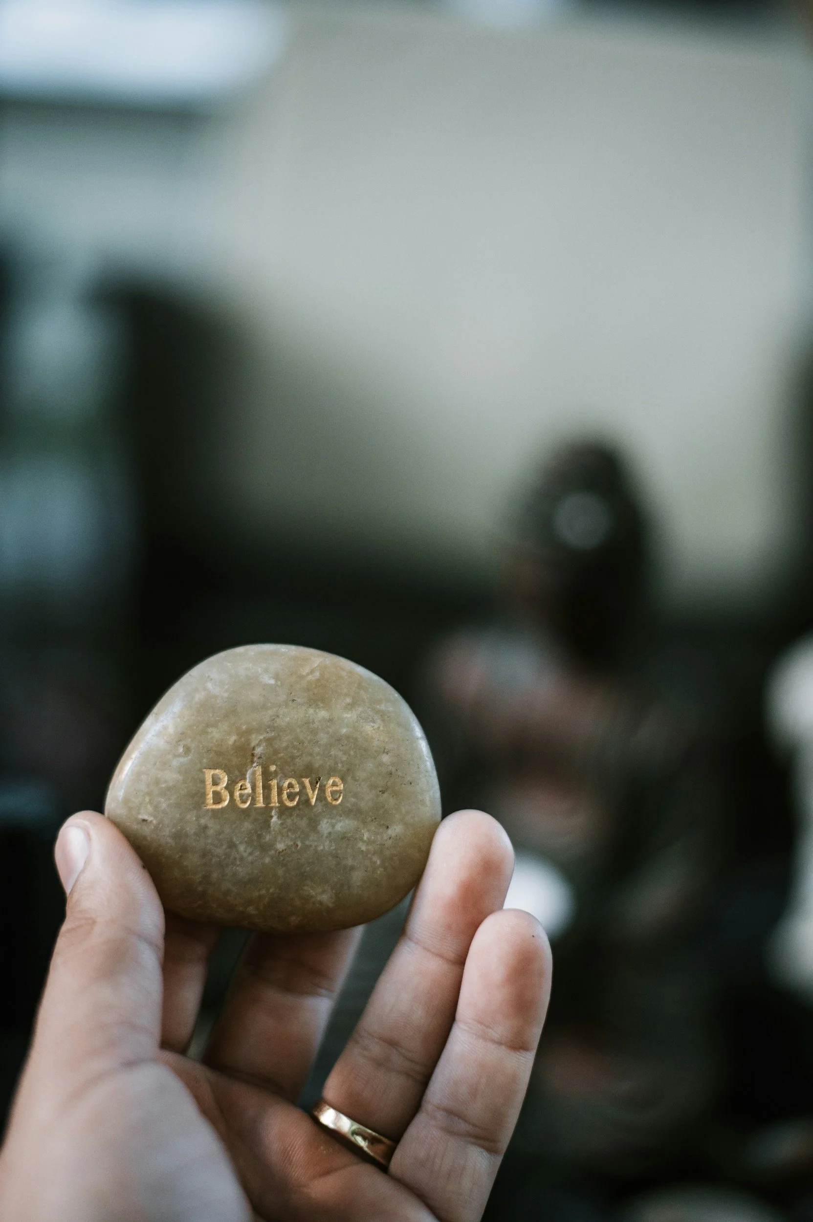 A hand holding a smooth, oval-shaped stone with the word "Believe" engraved on it.