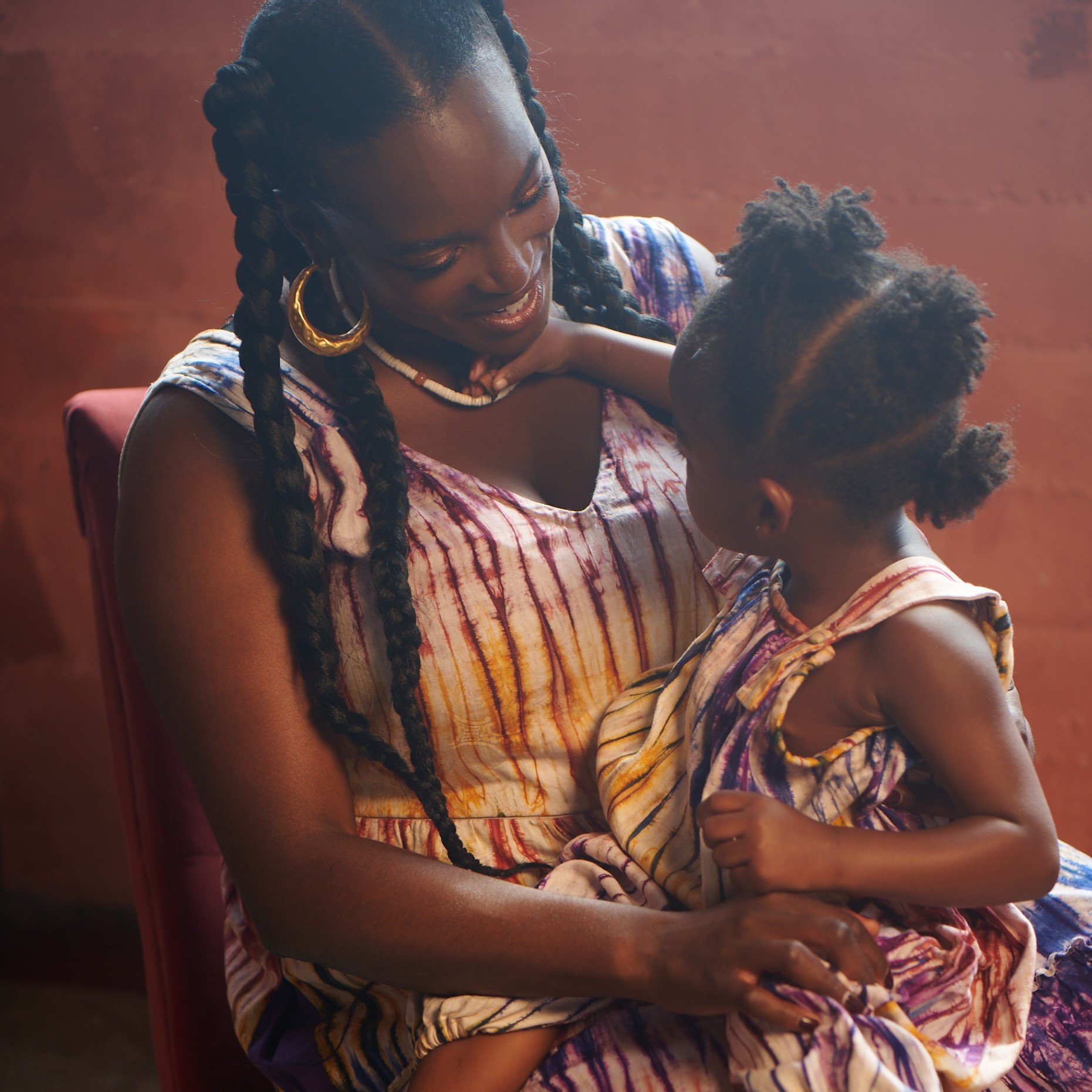 Wunmi cuddles her daughter in coordinating colorful patterned mother-and-child dresses.