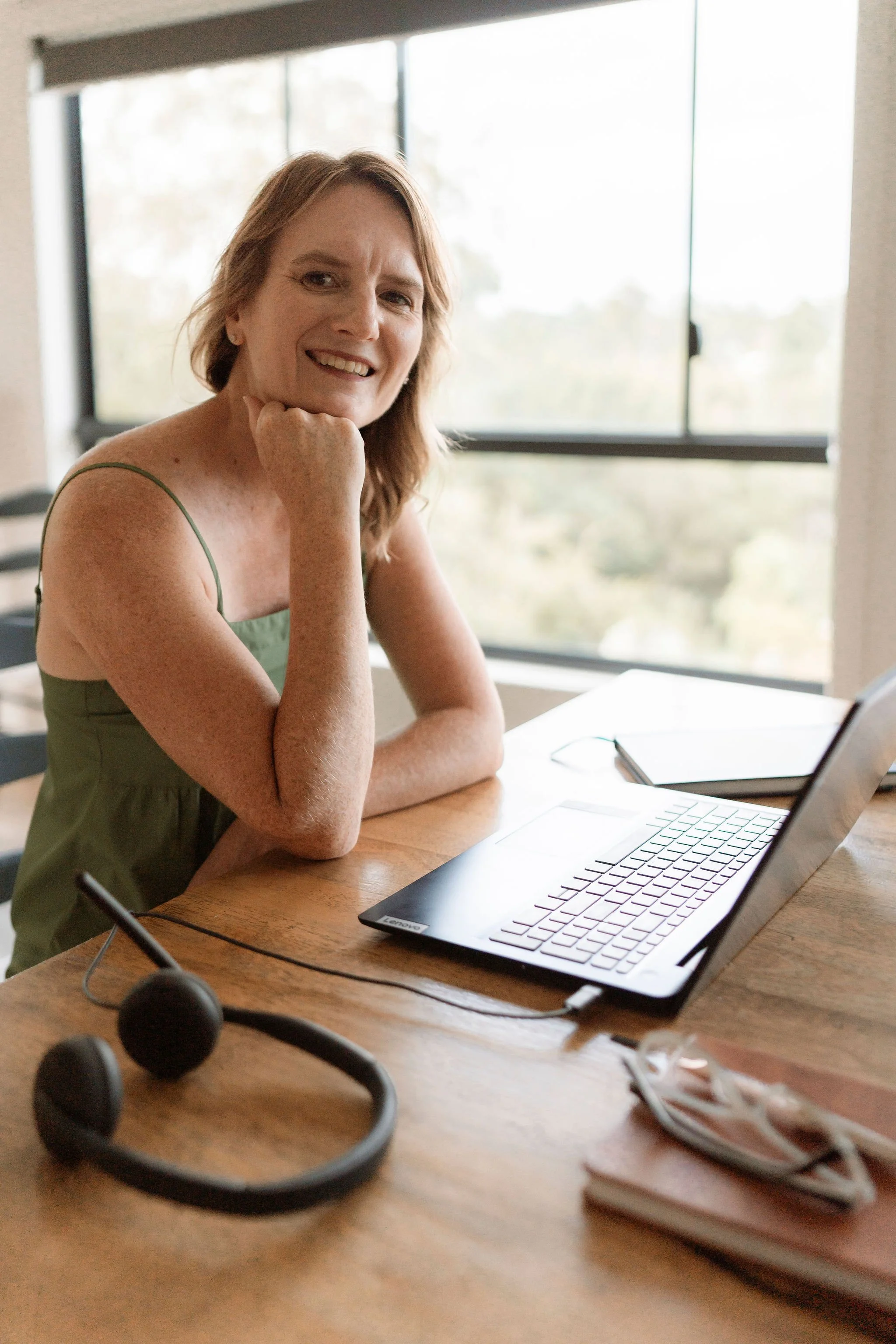 Woman smiling at a desk with a laptop and headset