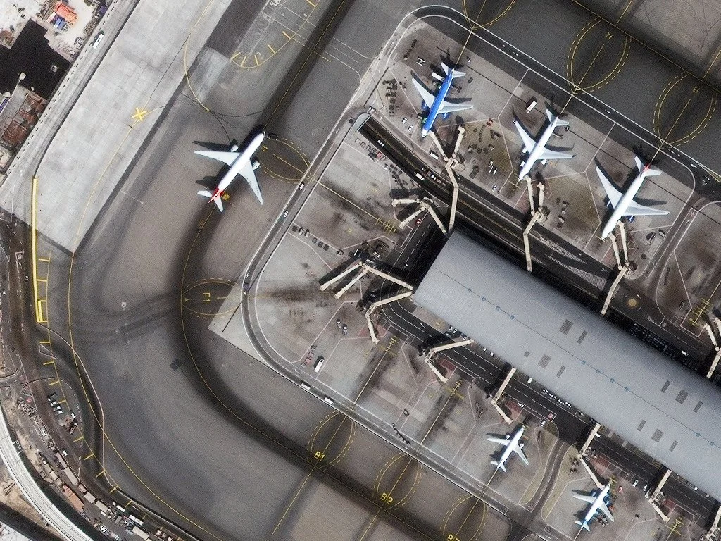 Aerial view of an airport showing multiple airplanes parked at gates and on the tarmac, with a jet bridge connecting to a terminal.