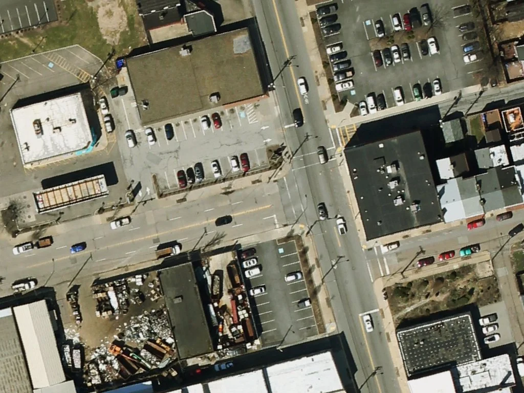 An aerial view of a downtown area with buildings, parking lots, and streets filled with cars.