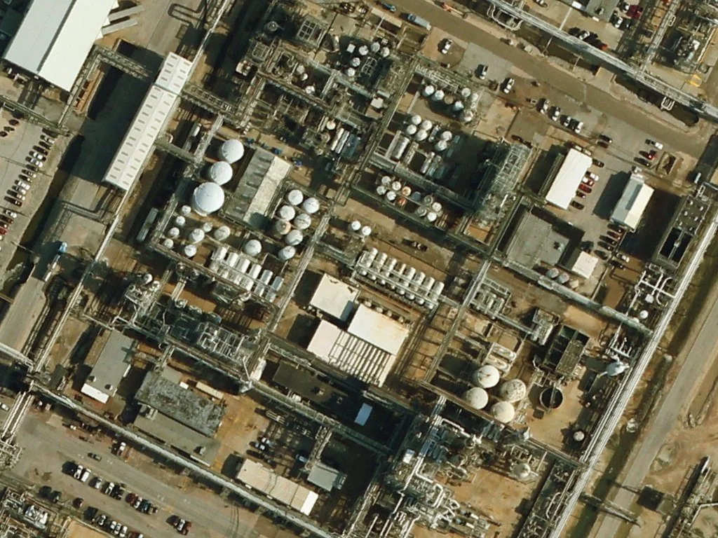 Aerial view of an industrial factory with multiple tanks, pipes, and buildings.