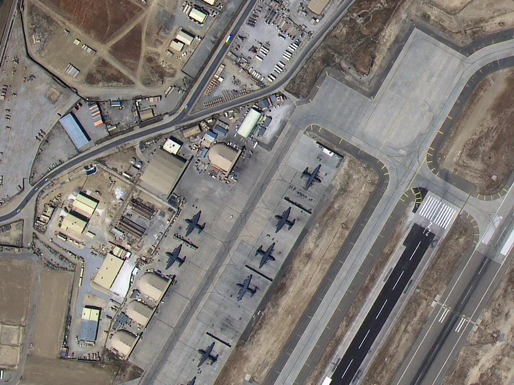 Satellite view of a military airbase with several parked fighter jets, runways, taxiways, and support buildings.