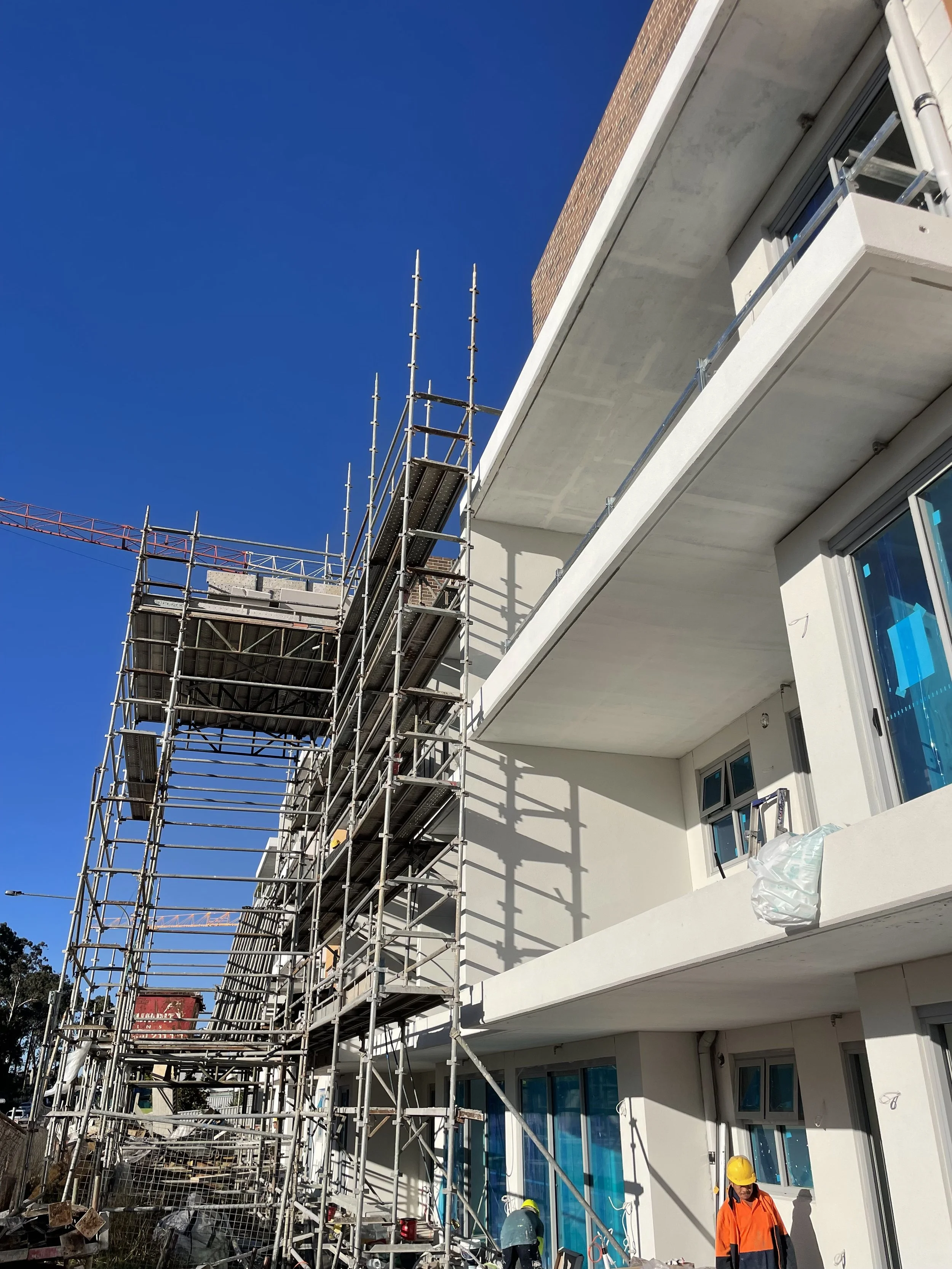 Construction workers shop building with steel scaffolding on a white multi-story building under a clear blue sky.