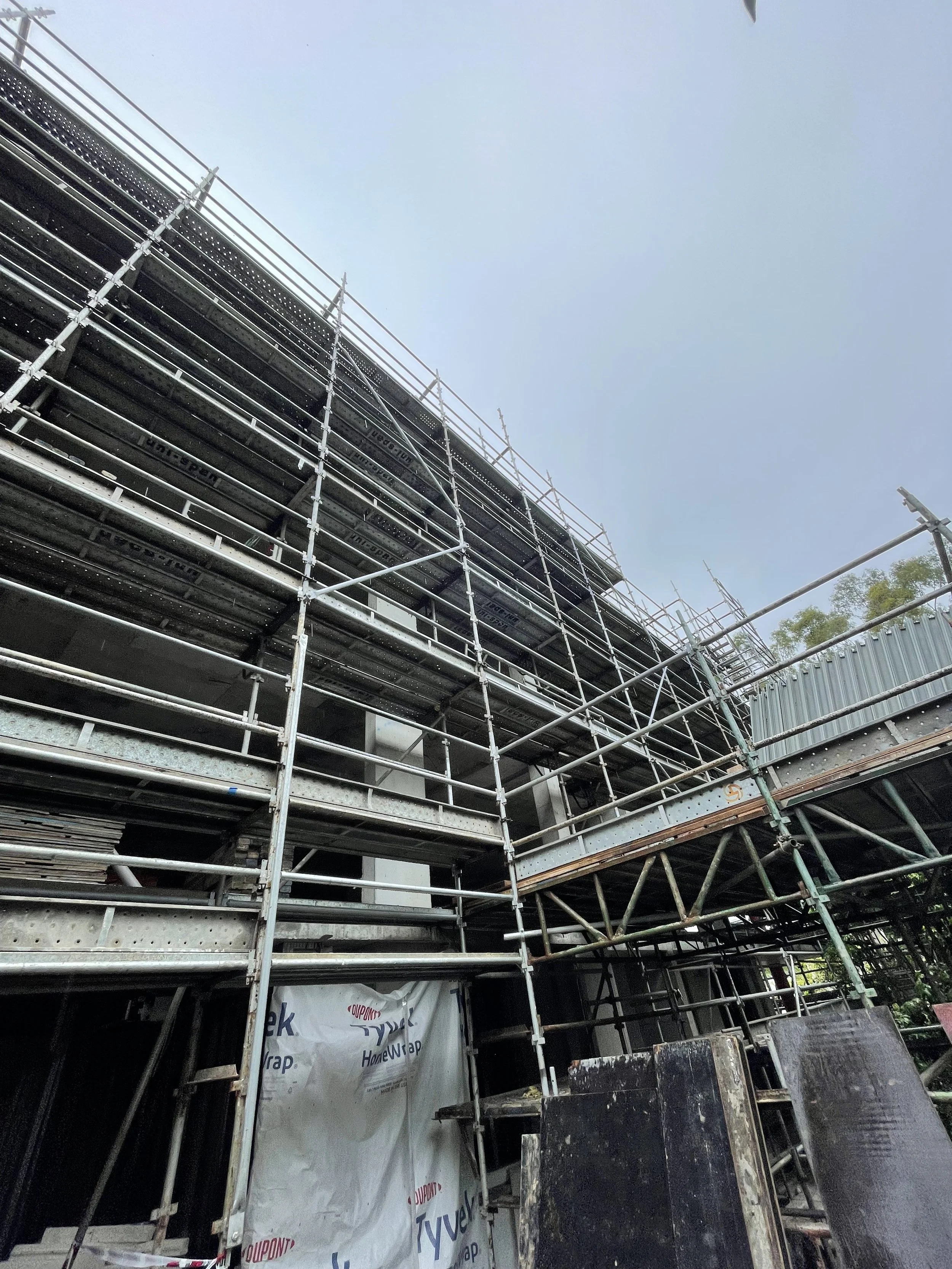 Construction site with multiple levels of metal scaffolding around a building under construction with a clear sky overhead.