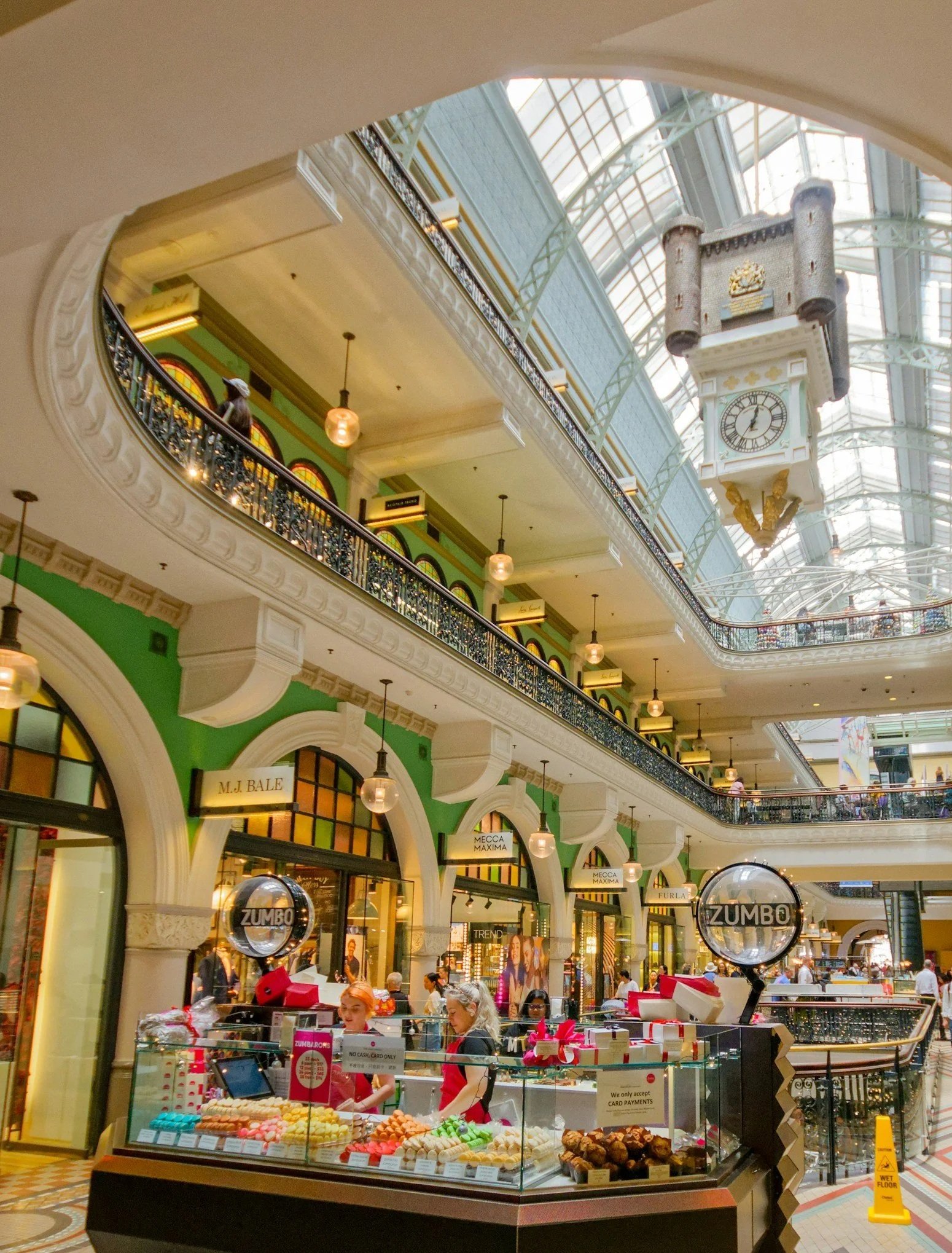 Interior of a shopping mall with a glass ceiling, standing storefronts, and a candy kiosk in the foreground.