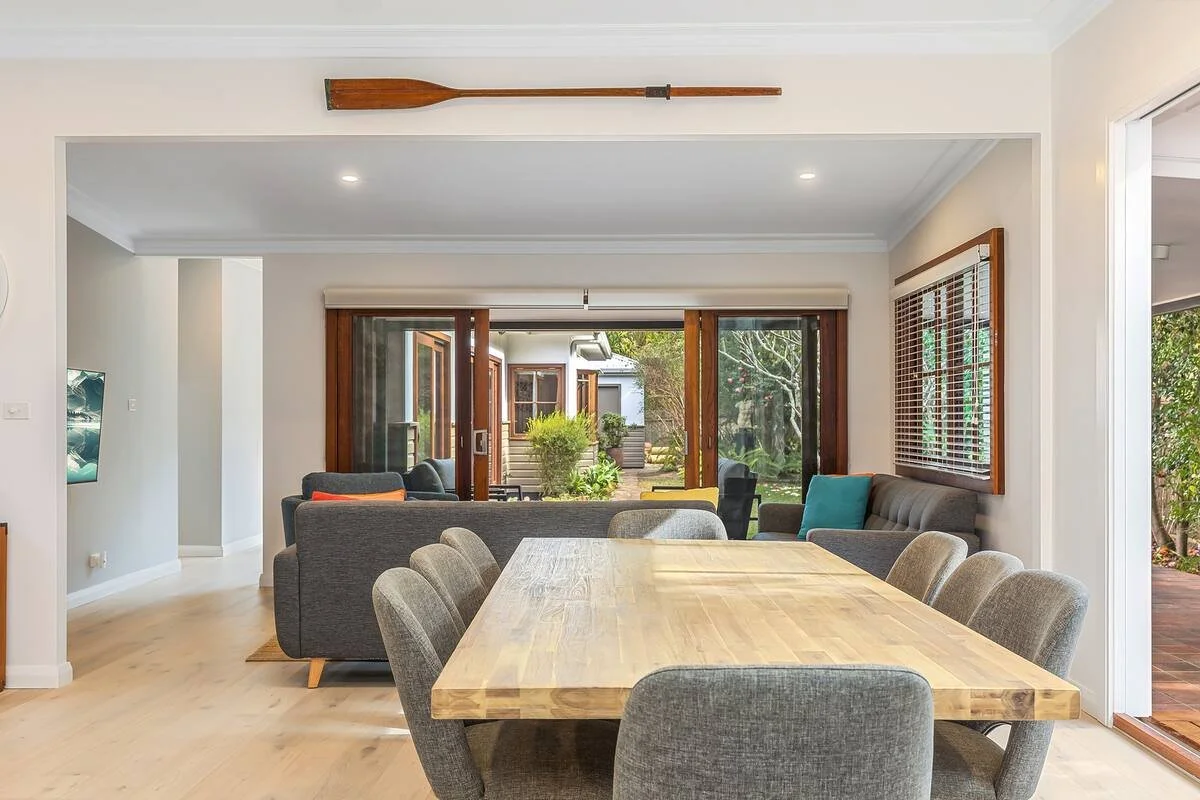 Dining room with a large wooden table, eight upholstered chairs, and a view of the sunny backyard through sliding glass doors.