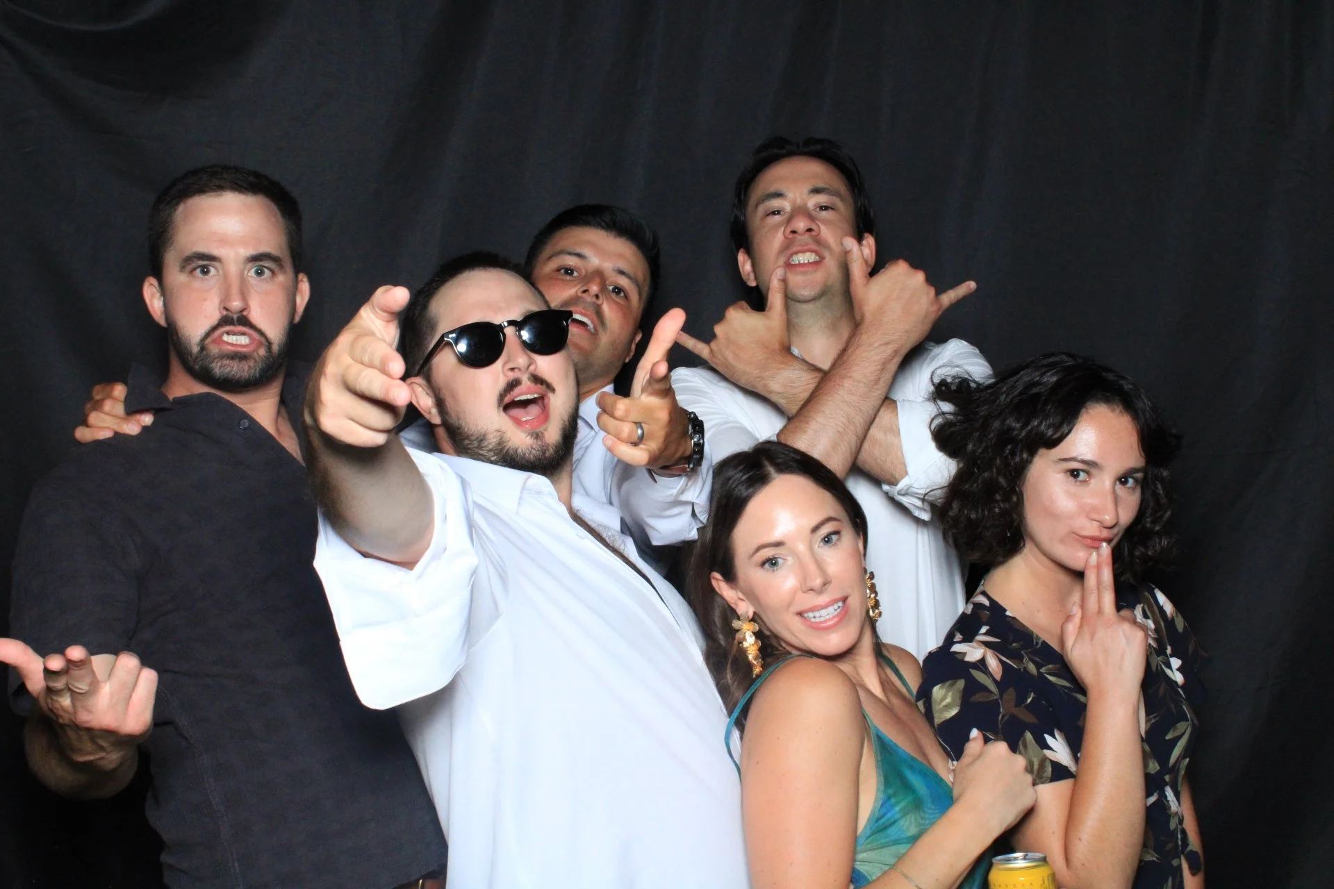 Group of six people posing together in front of a black backdrop, making various expressions and gestures.