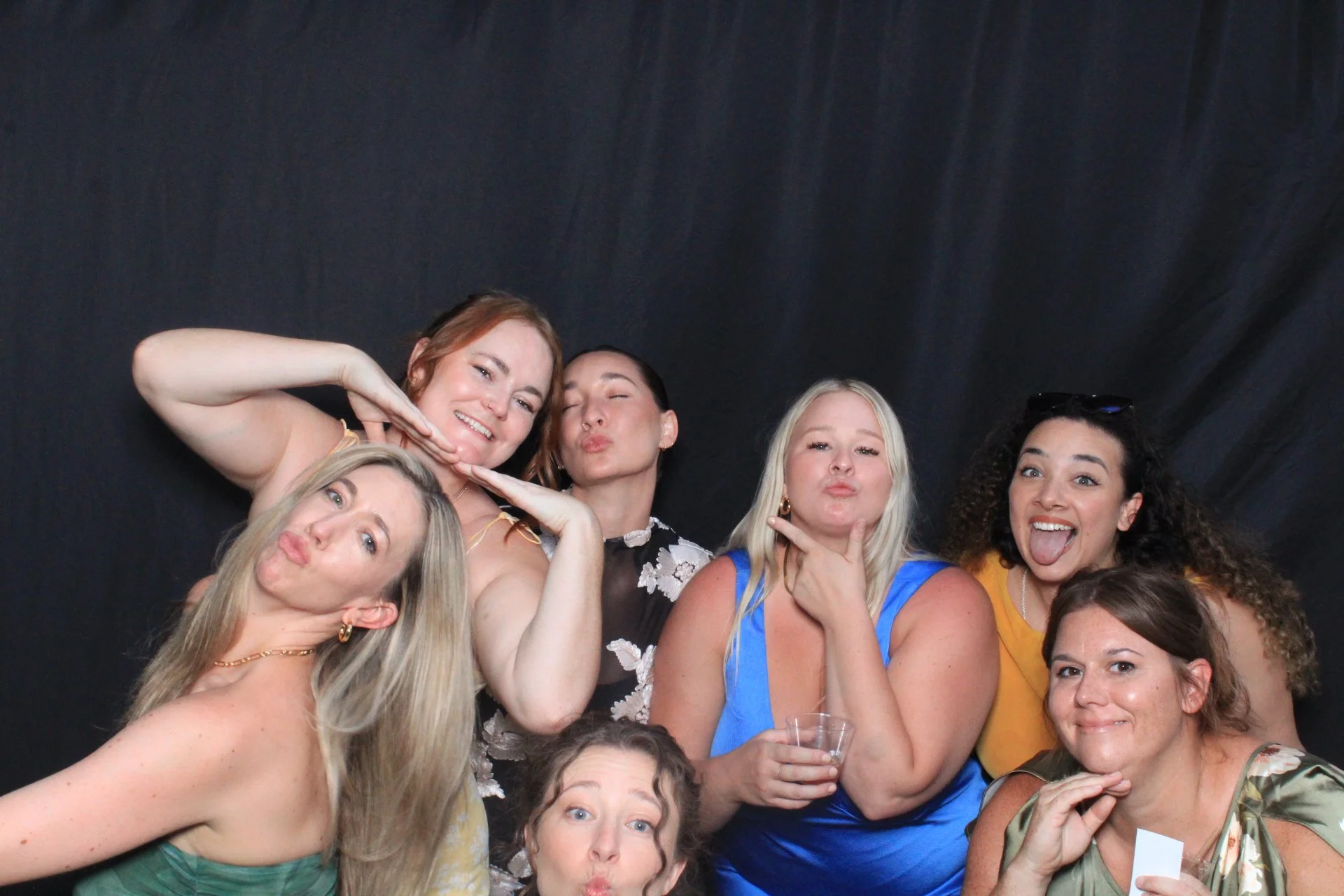 Group of women posing playfully at a photo booth with a dark background.