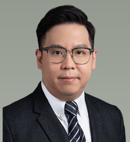 A professional headshot of a man with glasses, wearing a suit and tie, against a plain background.