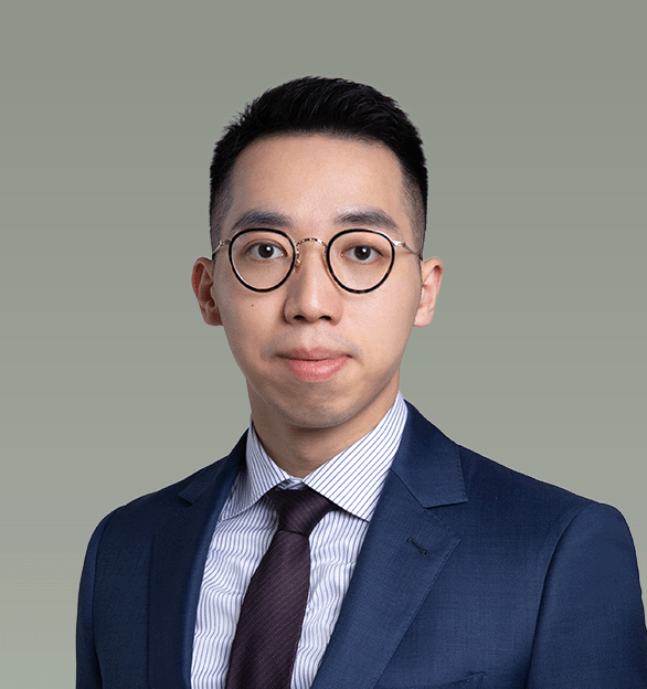Professional portrait of a young man in a blue suit, white striped shirt, and dark tie, wearing round glasses, with a neutral background.
