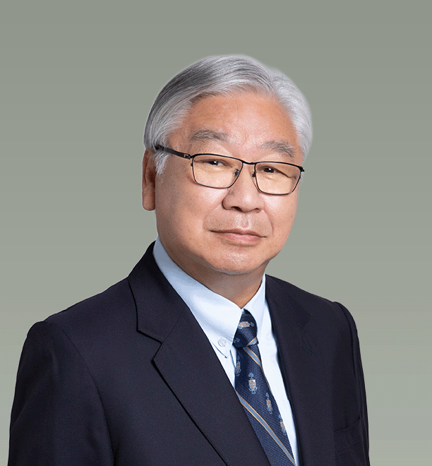 Portrait of an older Asian man with gray hair and glasses, wearing a dark suit, light blue shirt, and patterned tie, against a plain gray background.
