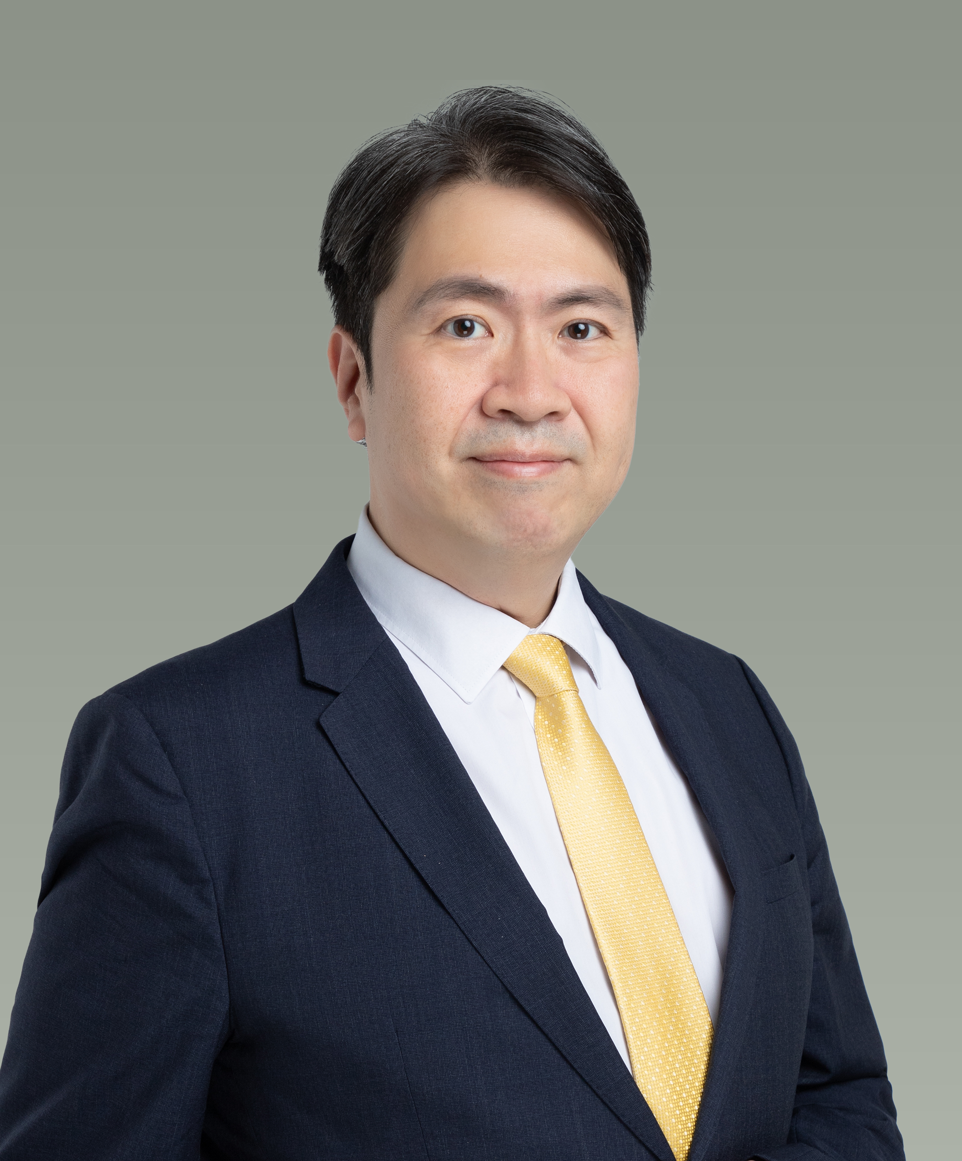 Professional headshot of a man in a dark suit, white shirt, and yellow tie, standing against a plain gray background.