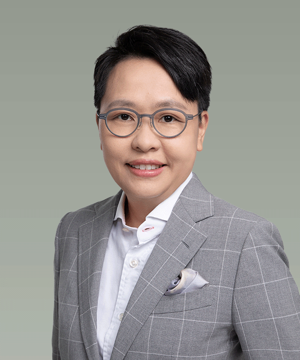 Portrait of a person wearing glasses, a light gray plaid blazer, and a white shirt with a pocket square, smiling against a plain muted green background.