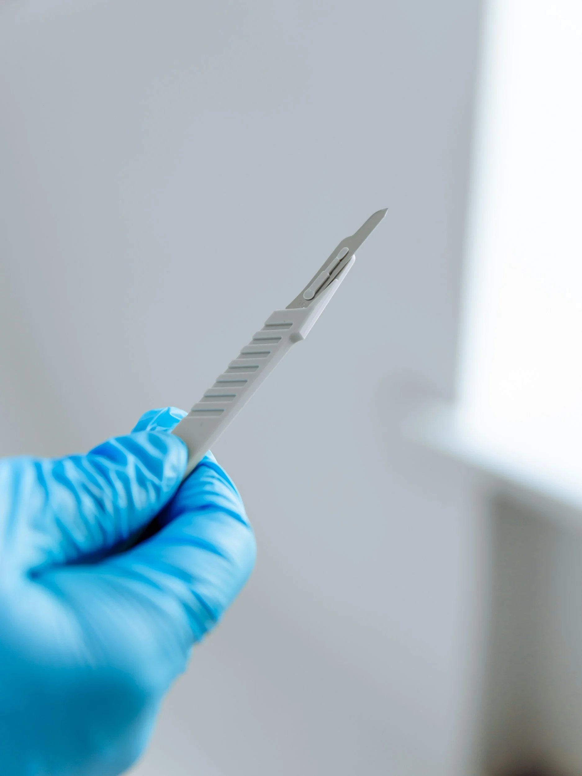 A gloved hand holding a medical scalpel against a plain background.