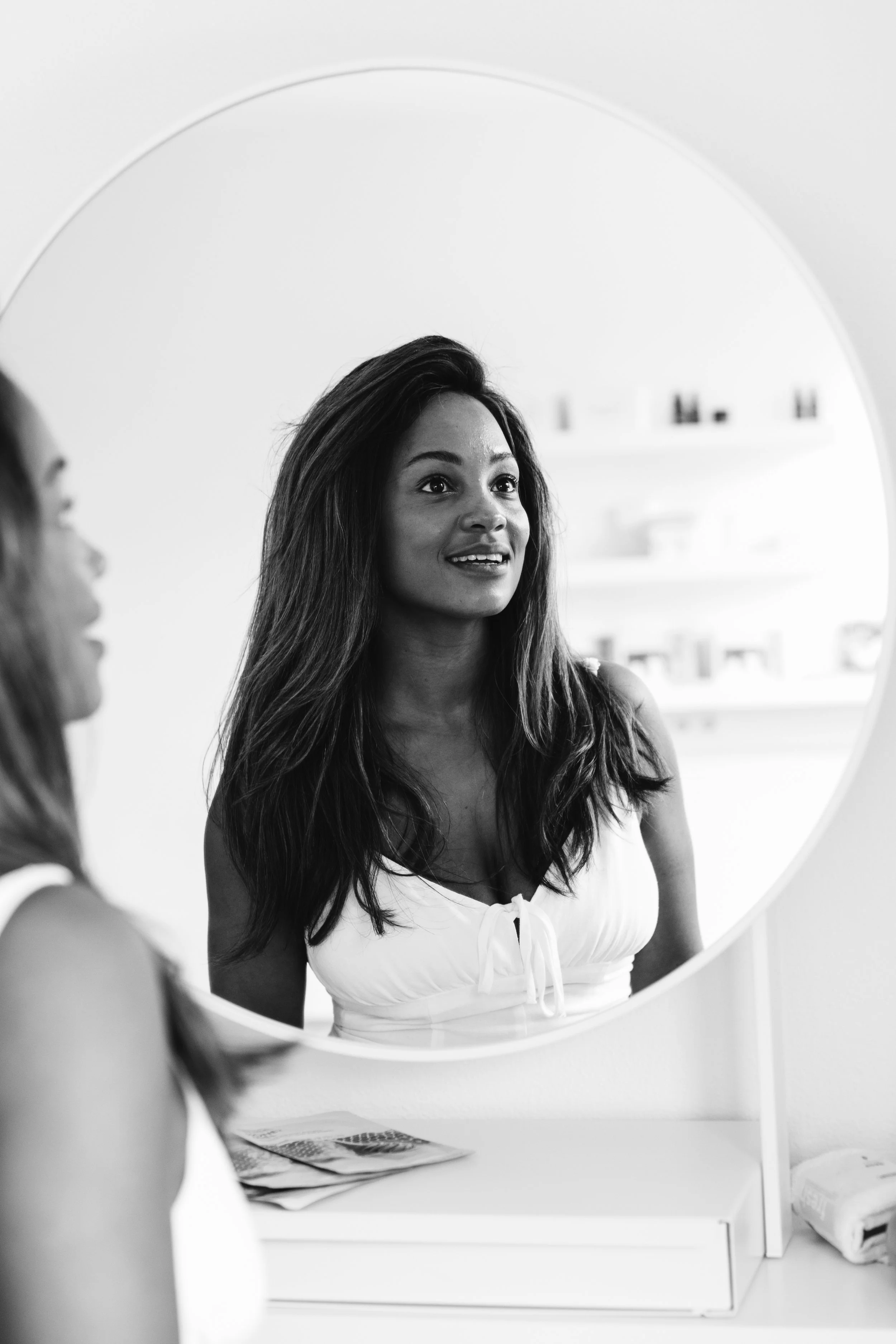 A woman Olive Andexer looking at herself in a mirror, smiling. The image is in black and white.