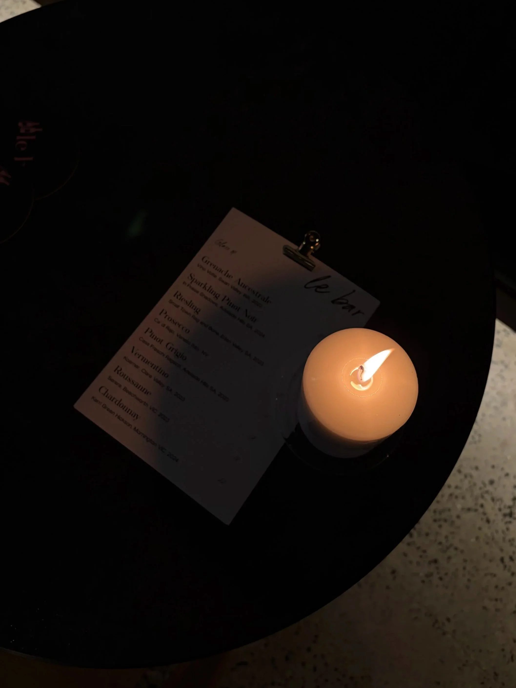 Lit candle on a black table, with a menu clipped to a black clipboard.