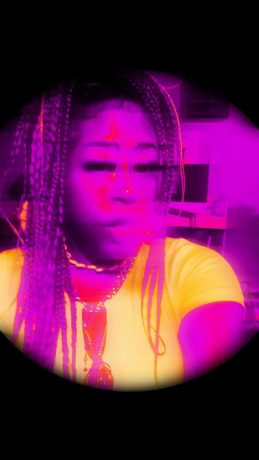 A woman with braided hair, wearing a yellow top, and multiple necklaces, taking a selfie with a purple and pink neon glow effect.