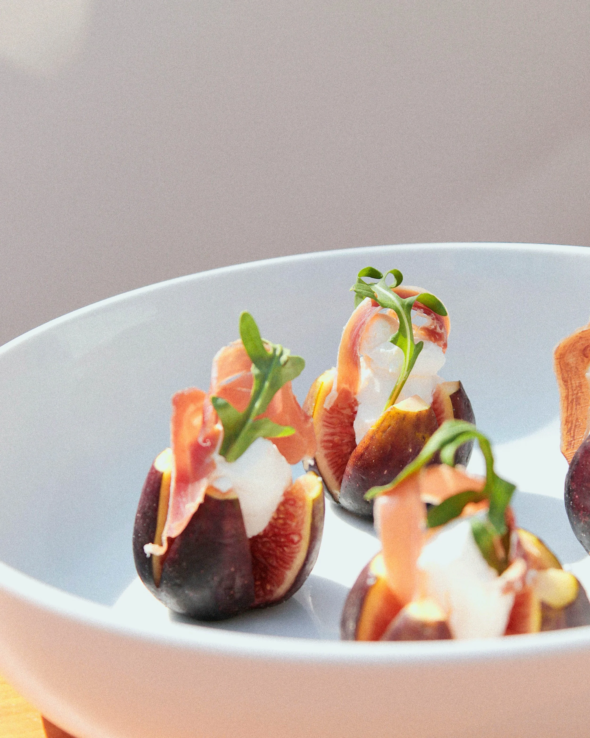 Feuilles de microgreens, figues, fromage, jambon cru et crackers dans un bol blanc.