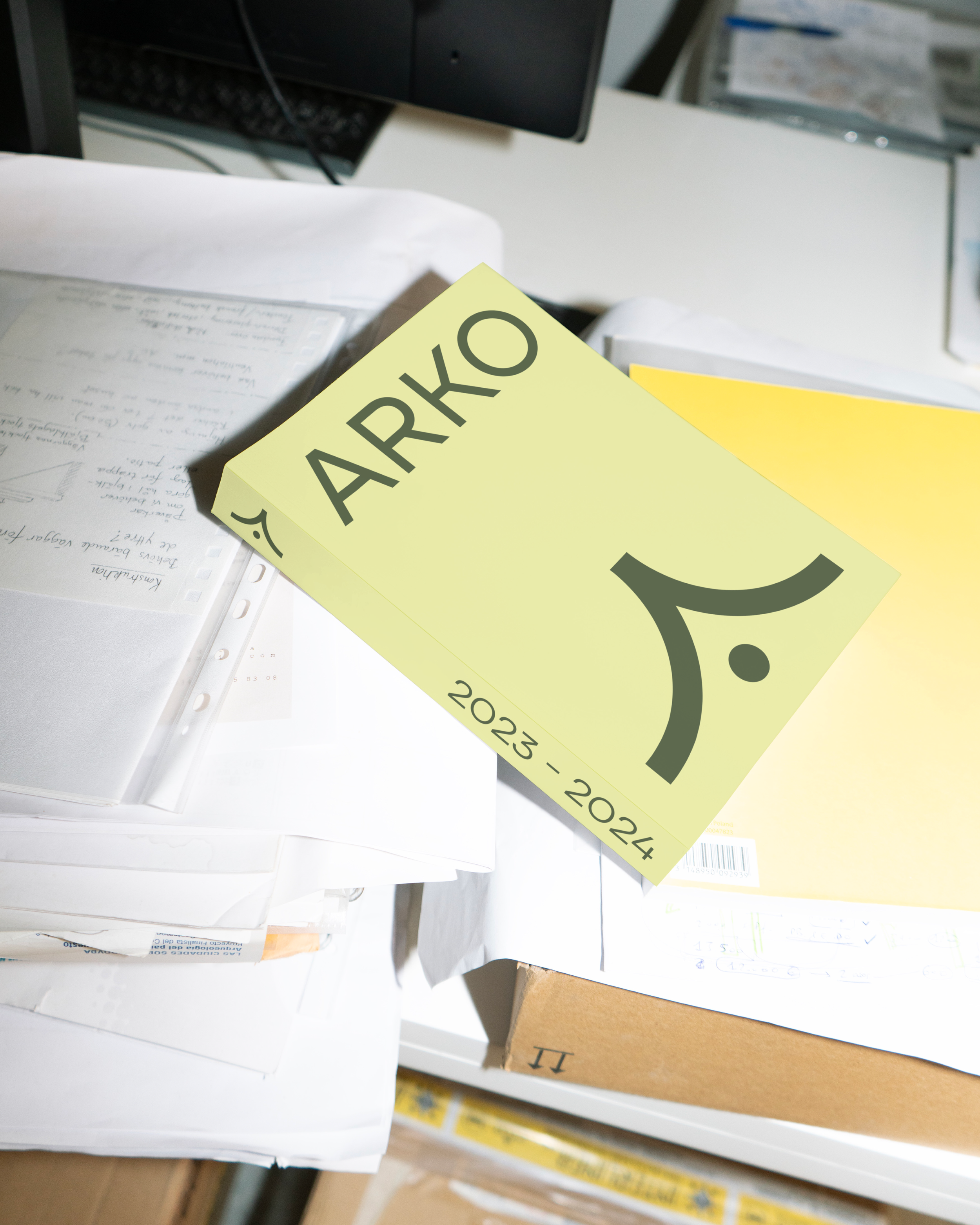 Une pile de papiers et de notebooks sur un bureau avec un marque-page jaune portant la mention 'ARHO' et les dates 2023-2024.