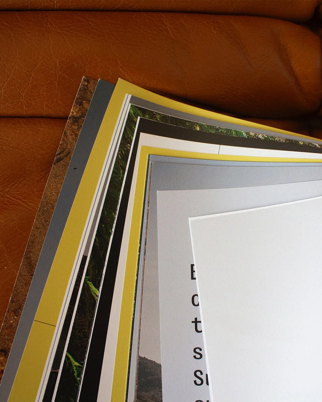 Une pile de magazines ou de brochures posée sur un canapé en cuir marron.