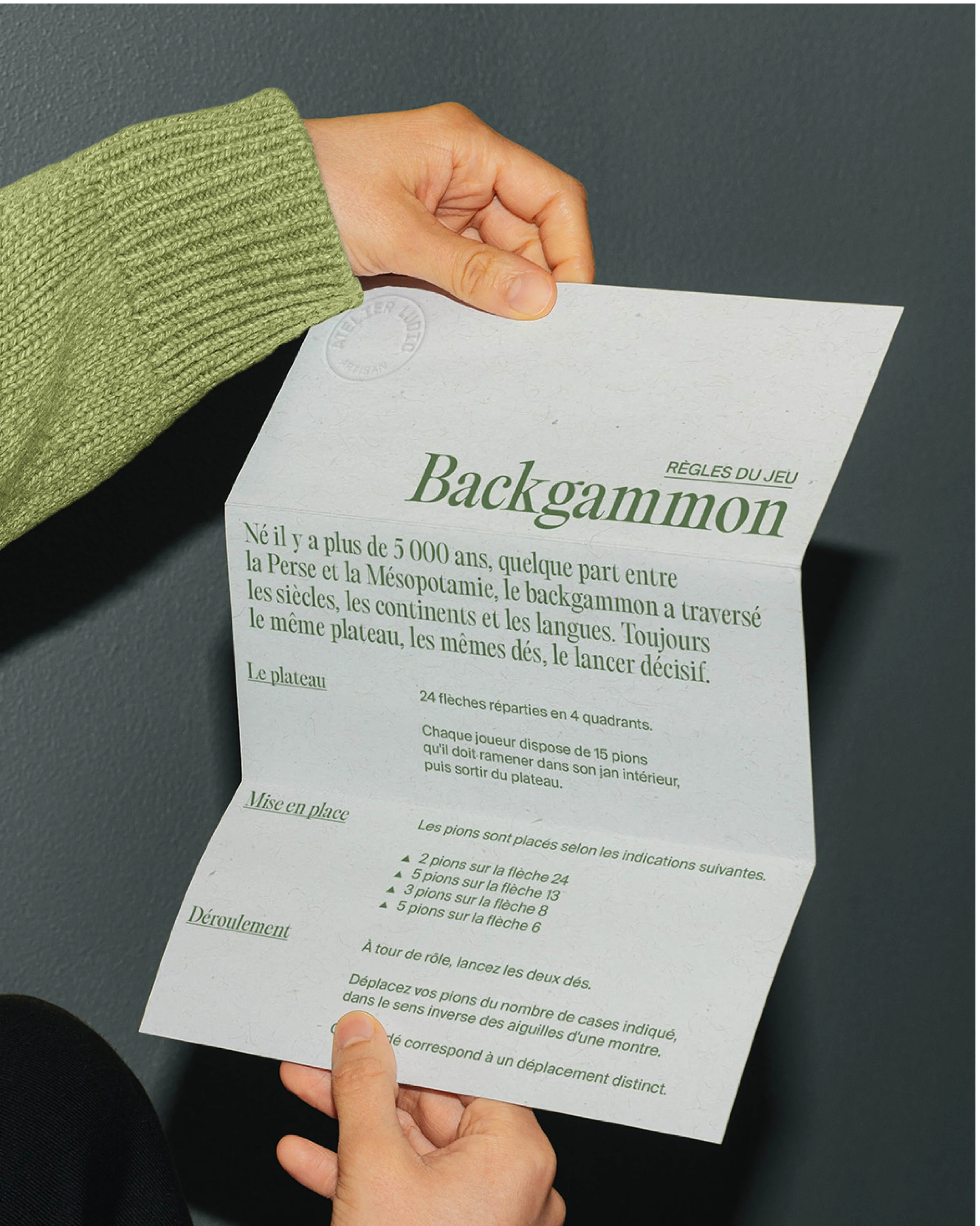 Une personne tient une feuille de papier avec des règles du jeu Backgammon écrites dessus.