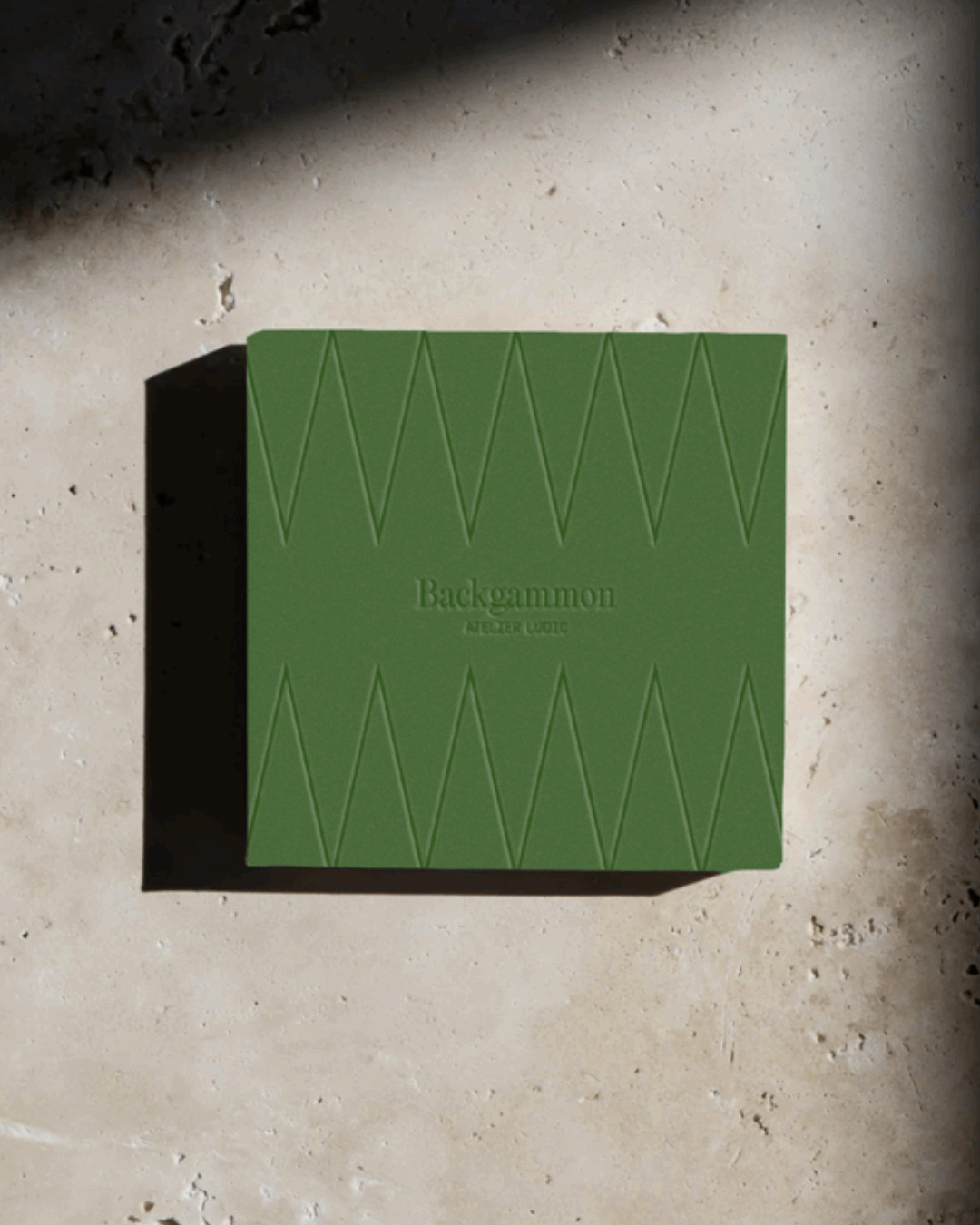 Une boîte verte de Backgammon posée sur une surface en pierre, avec un motif en forme de triangles sur le haut et le bas.