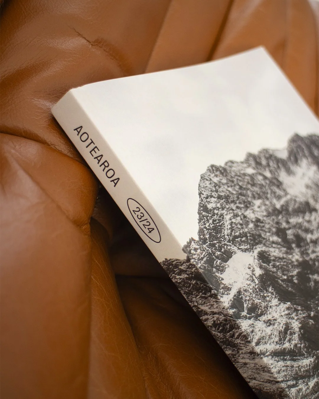 Une main tenant une boîte en carton blanc avec une image noire et blanche de montagnes et le texte « AOTEAROA » et la date « 23/24 »