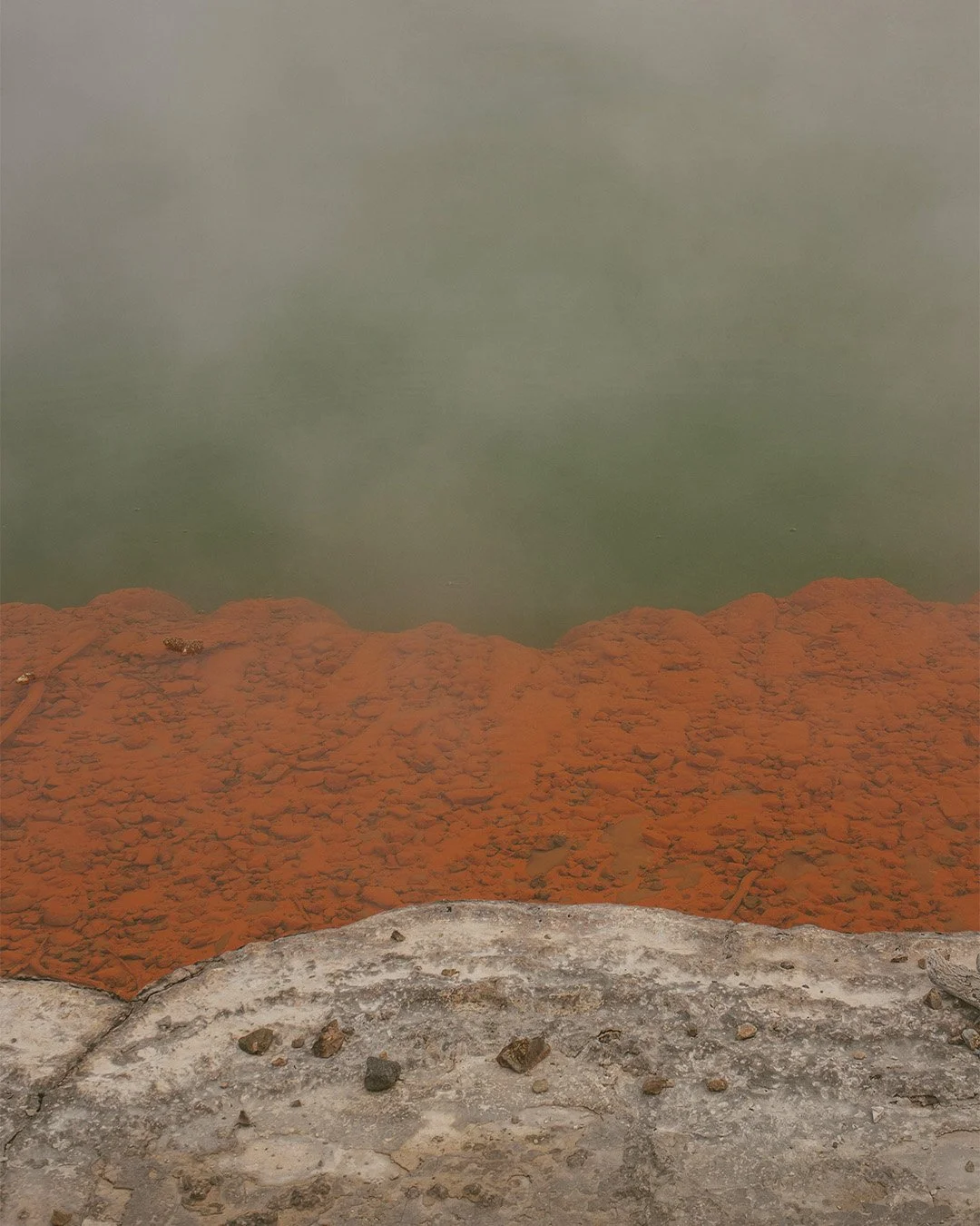 Photo d'une source géothermique avec de l'eau chaude de couleur verte et une zone environnante de sol avec un dépôt d'argile ou de minerai orange