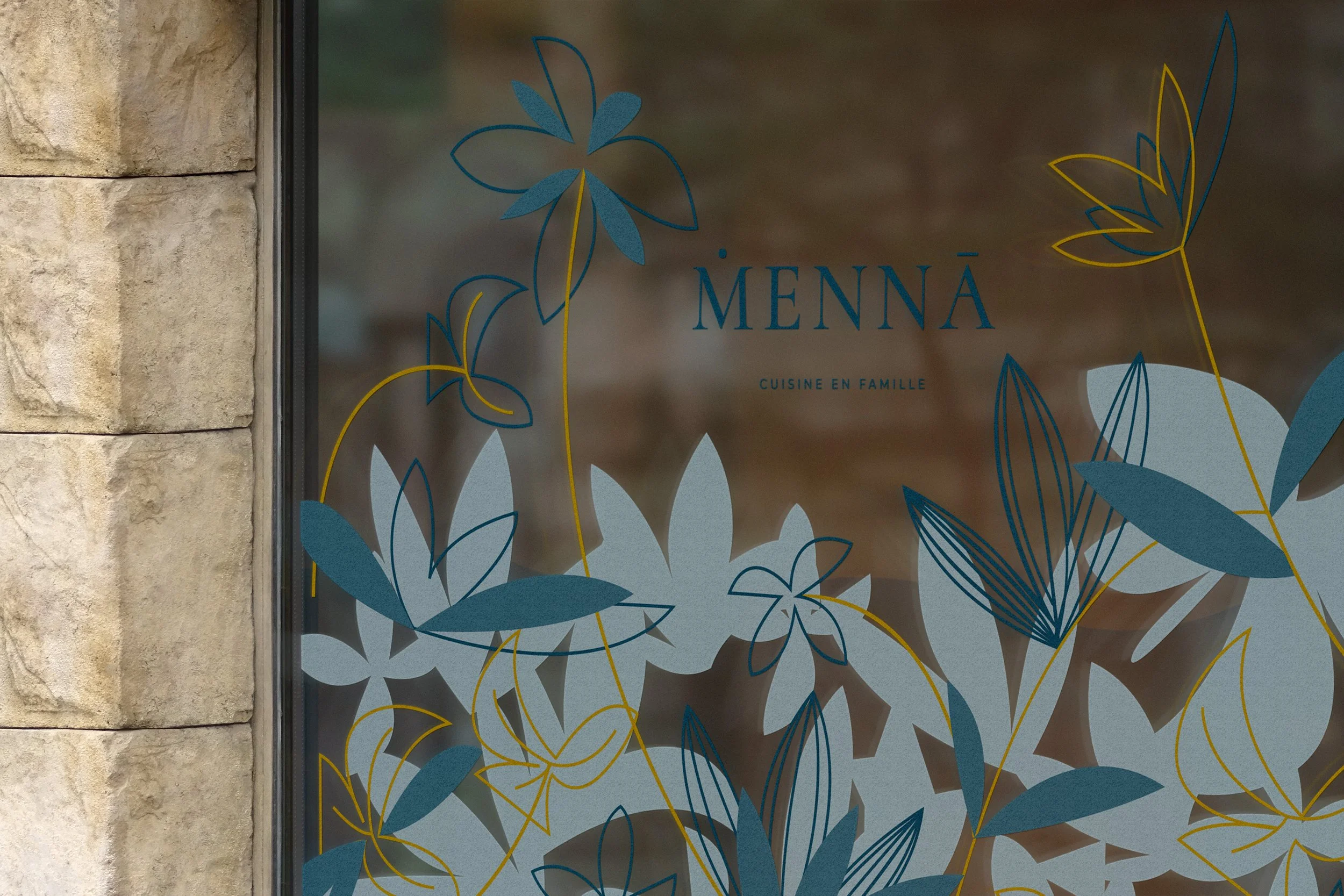 Fenêtre d'un restaurant nommé MENNÀ avec une décoration de fleurs stylisées en lignes bleues, jaunes et blanches, et le texte 'CUISINE EN FAMILLE'.