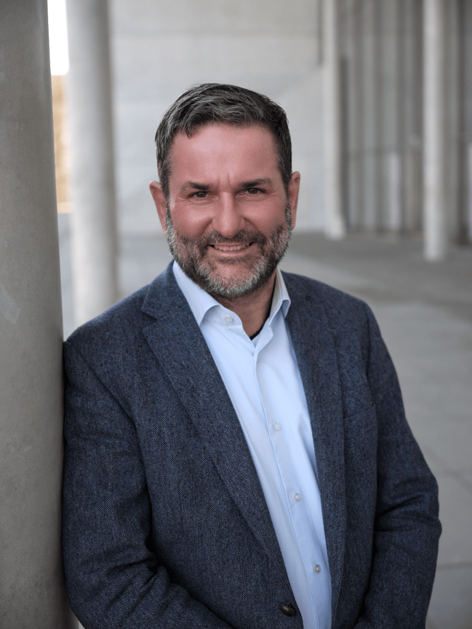 Mann mit blauem Hemd und dunkelblauem Sakko lehnt an grauer Säule, Sinnbild für mentale Gesundheit, Resilienz und Burnout-Prävention in München