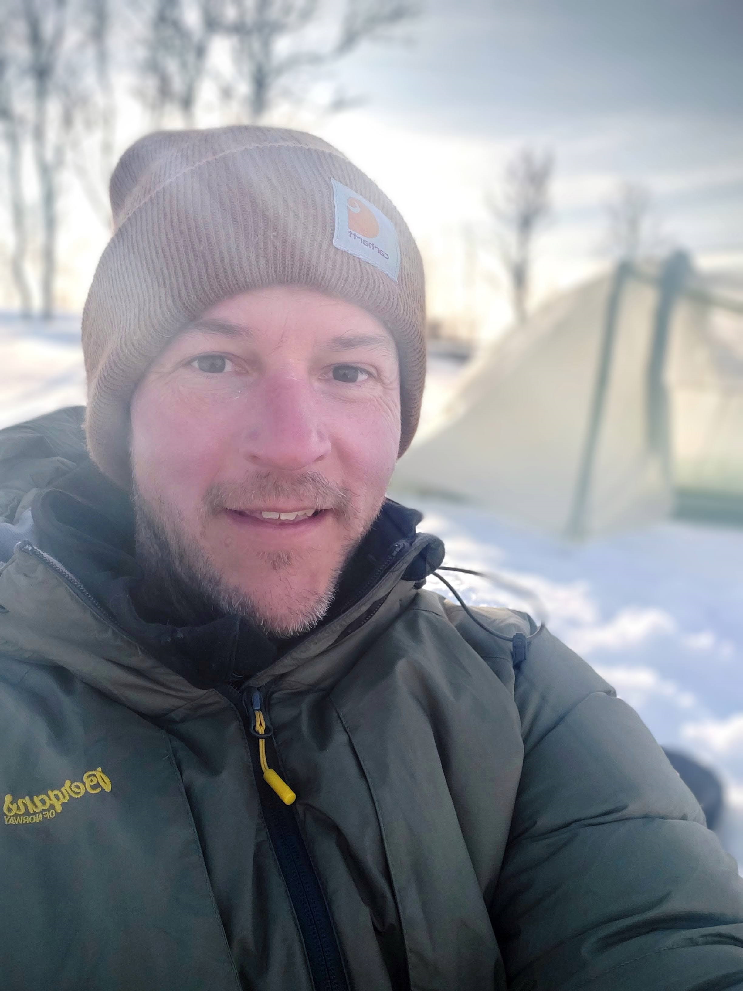 Earthling hiking guide camping near Tromsø wearing a brown beanie and green jacket.