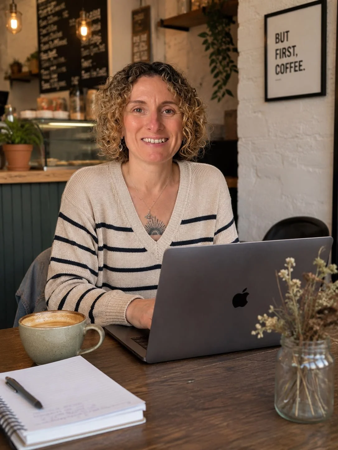Woman with curly hair and a striped sweater working on a laptop in a cozy café.