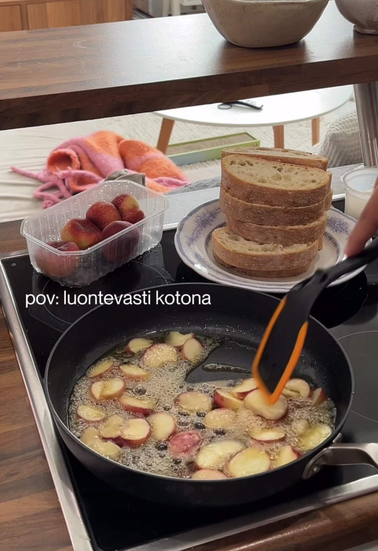 Paistinpannu, jossa on viipaloituja persikoita kiehumassa agavesiirapissa. Vieressä valkoinen lautanen, jonka päällä on paljon leipiä sekä rasia, jossa on kokonaisia persikoita.