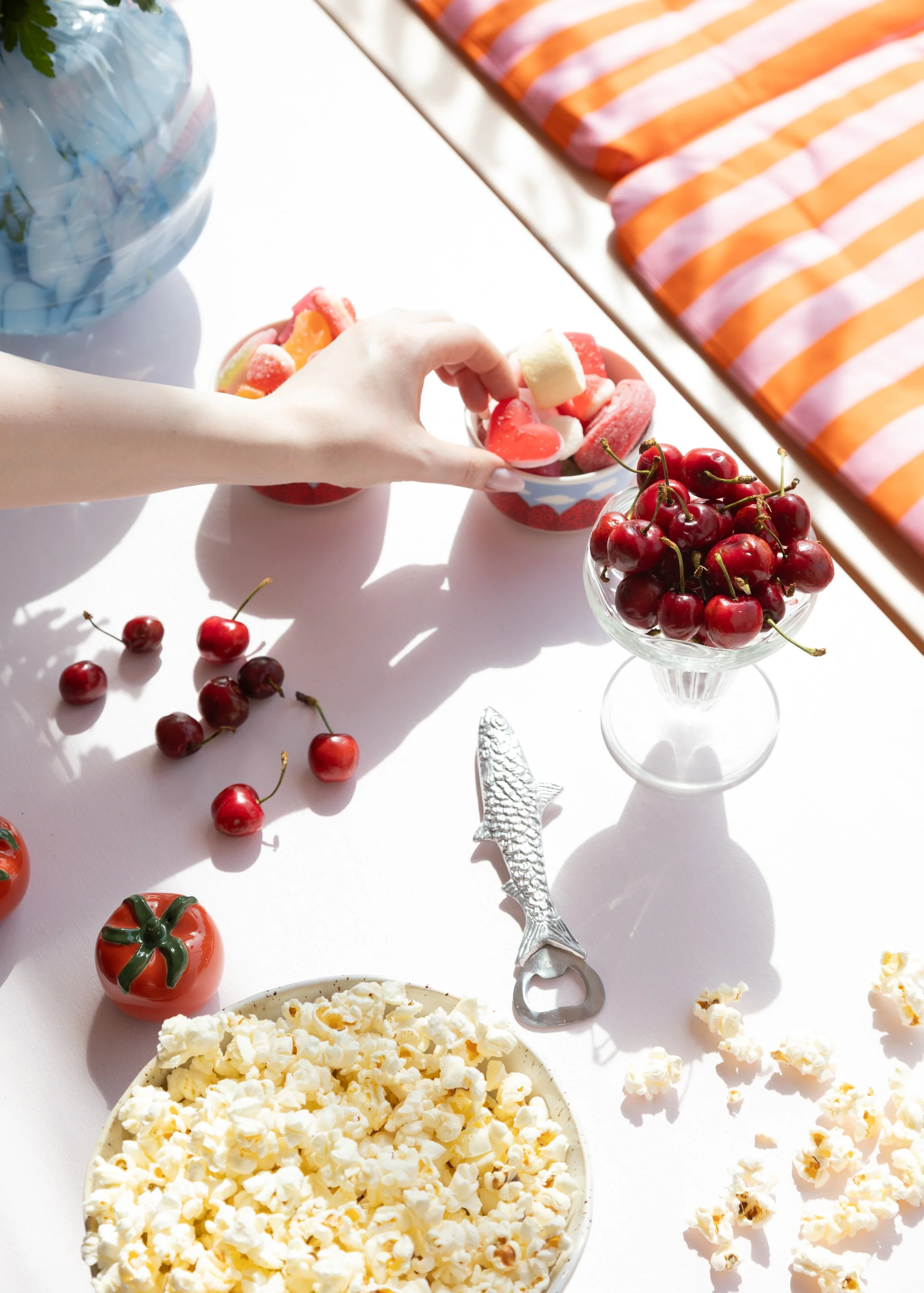 Pöytä, jossa on erilaisia herkkuja, kuten kirsikoita, karkkeja, popcornia.