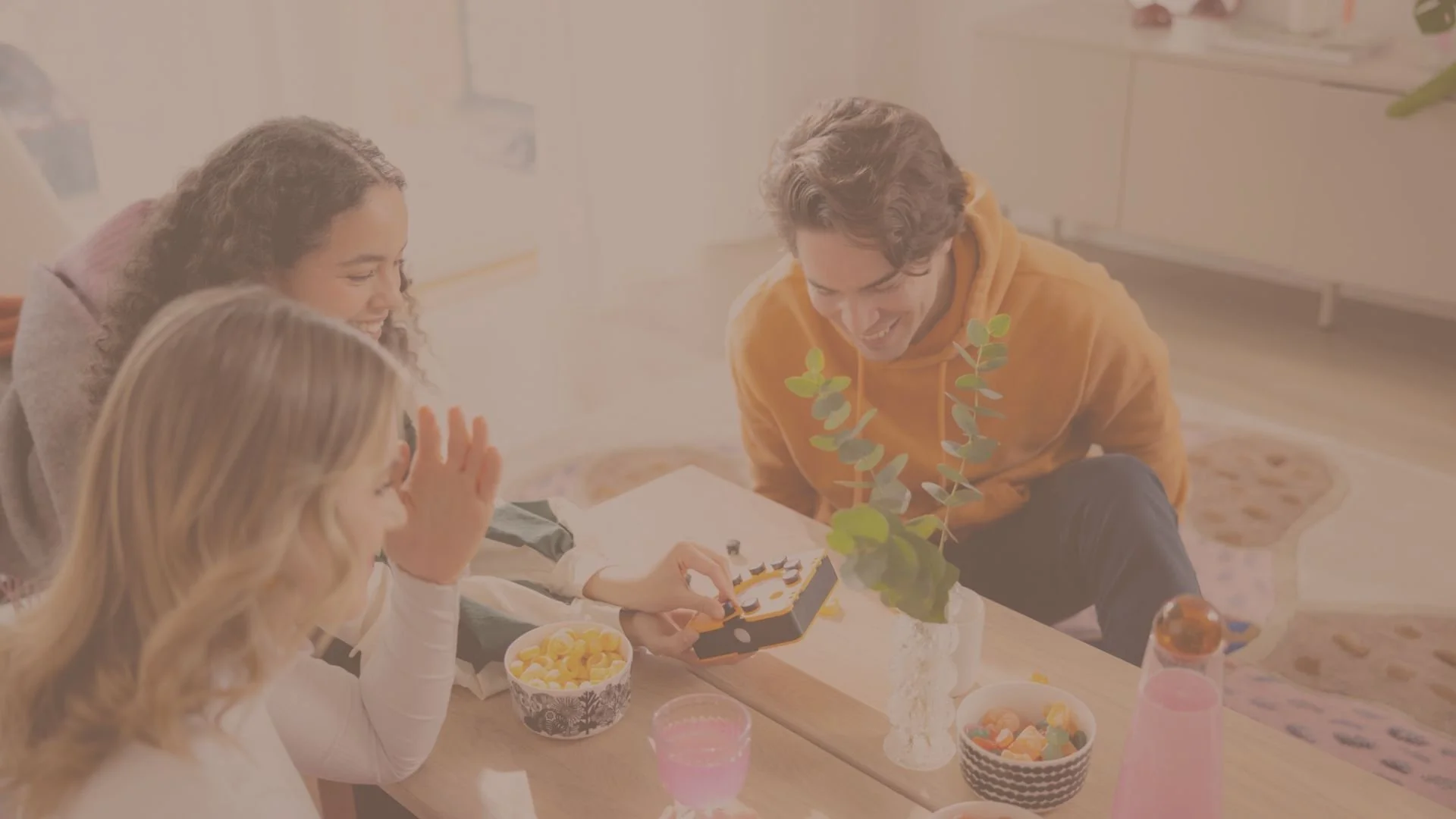 Kolme ihmistä nauttimassa aamupalaa ja pelaamassa lautapeliä pöydän ääressä.