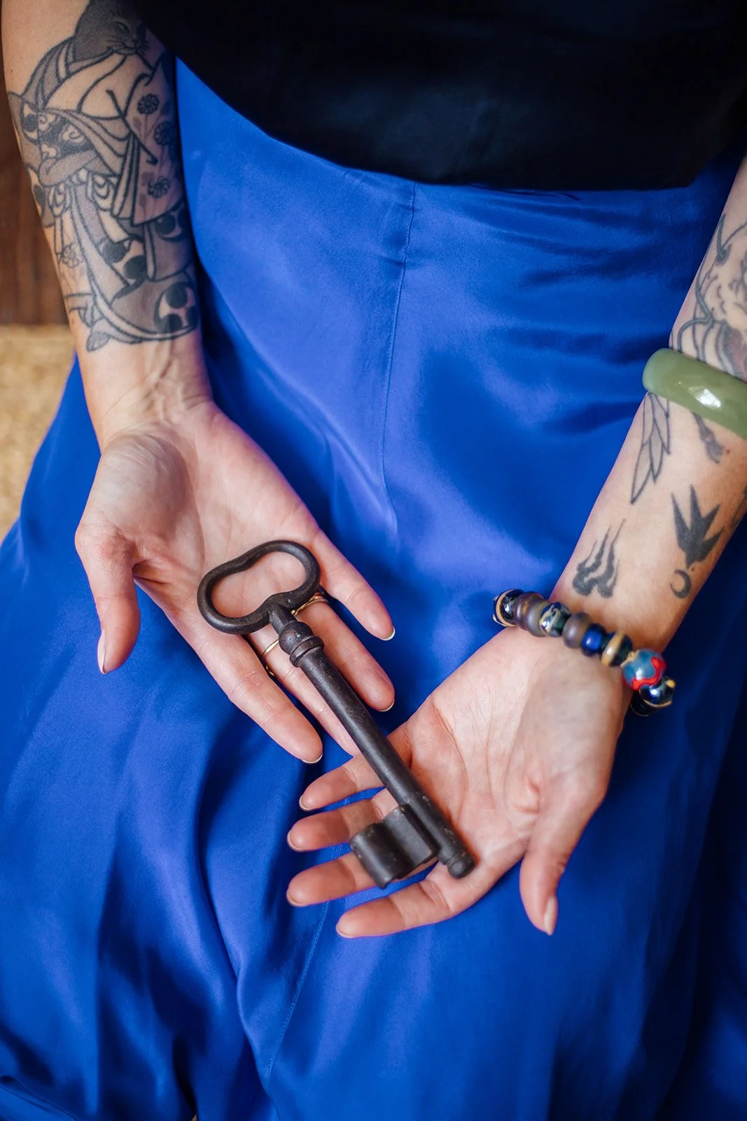 Persoon houdt een oud ijzeren sleutel vast, met tattoos op beide armen, zittend op een blauwe kleding