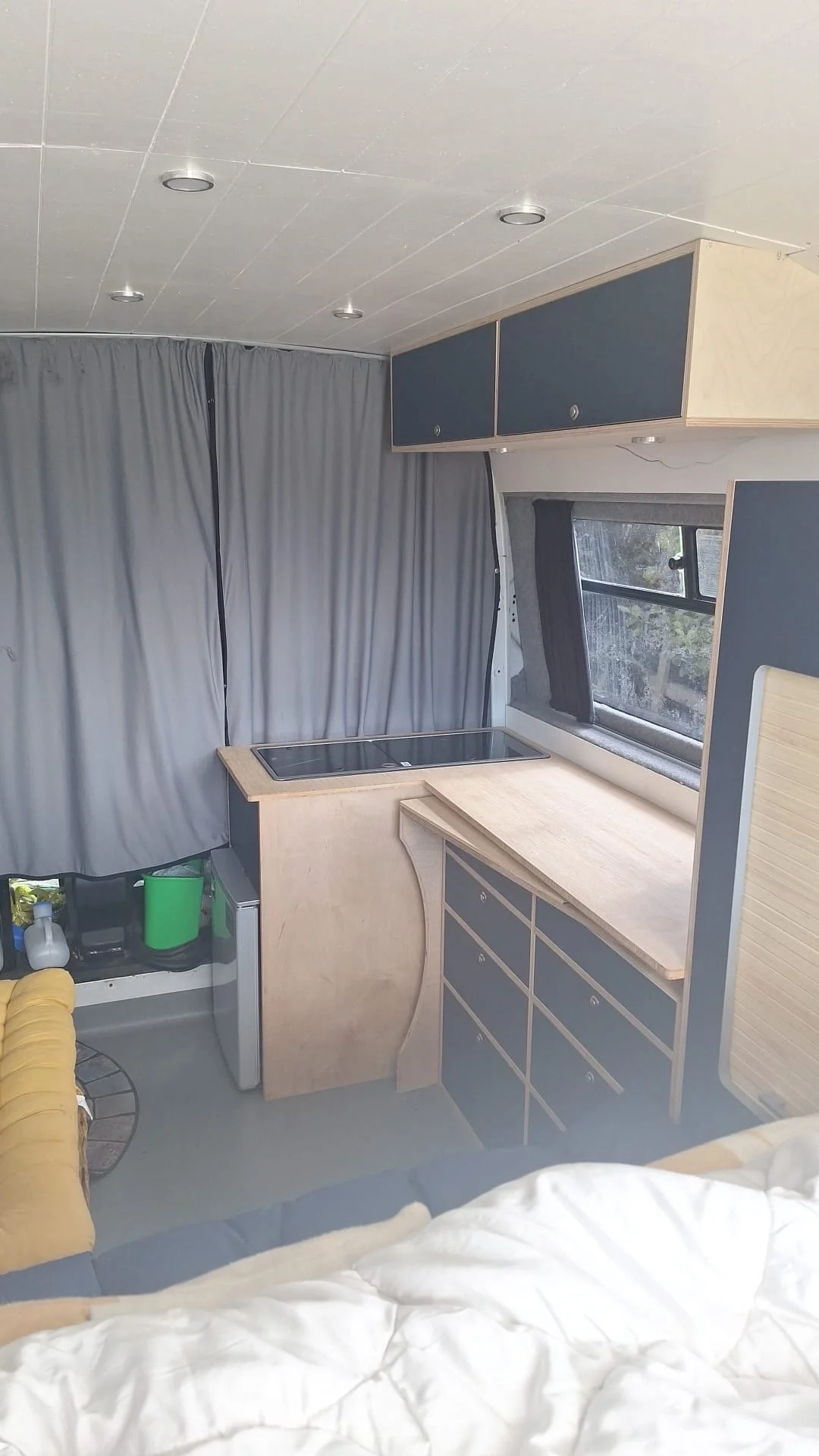 Interior of a small kitchen area in a camper or small living space with a window, cabinets, and a countertop with a sink.