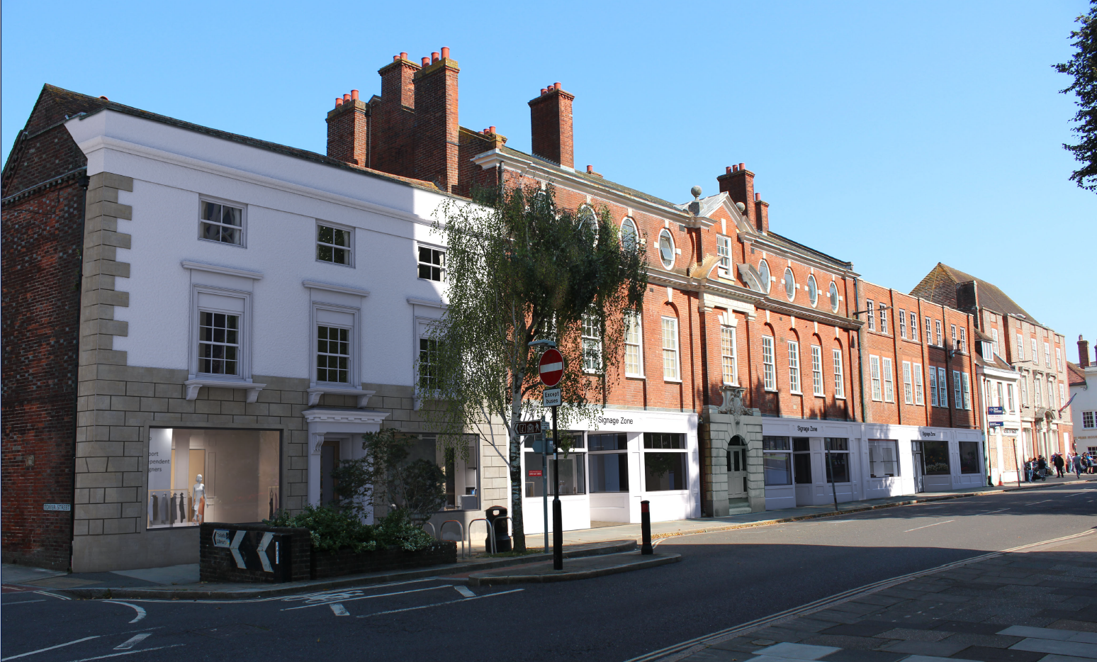 A street view of a historic red brick building with white architectural details, large windows, and a modern storefront at the ground level, under a clear blue sky.