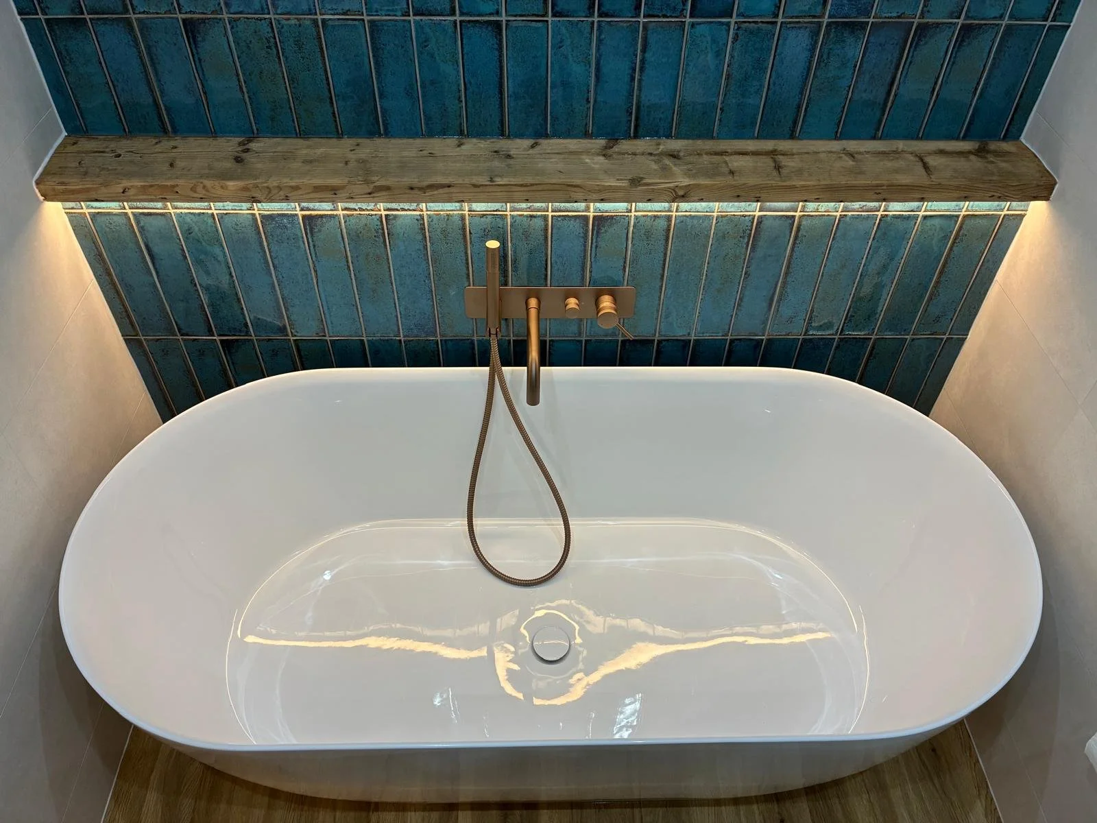 Incredible window display featuring feature tiles in a green herringbone behind a double vanity unit, a central free standing bath, and deluxe walk in shower area with leaf patterned tiles behind. 