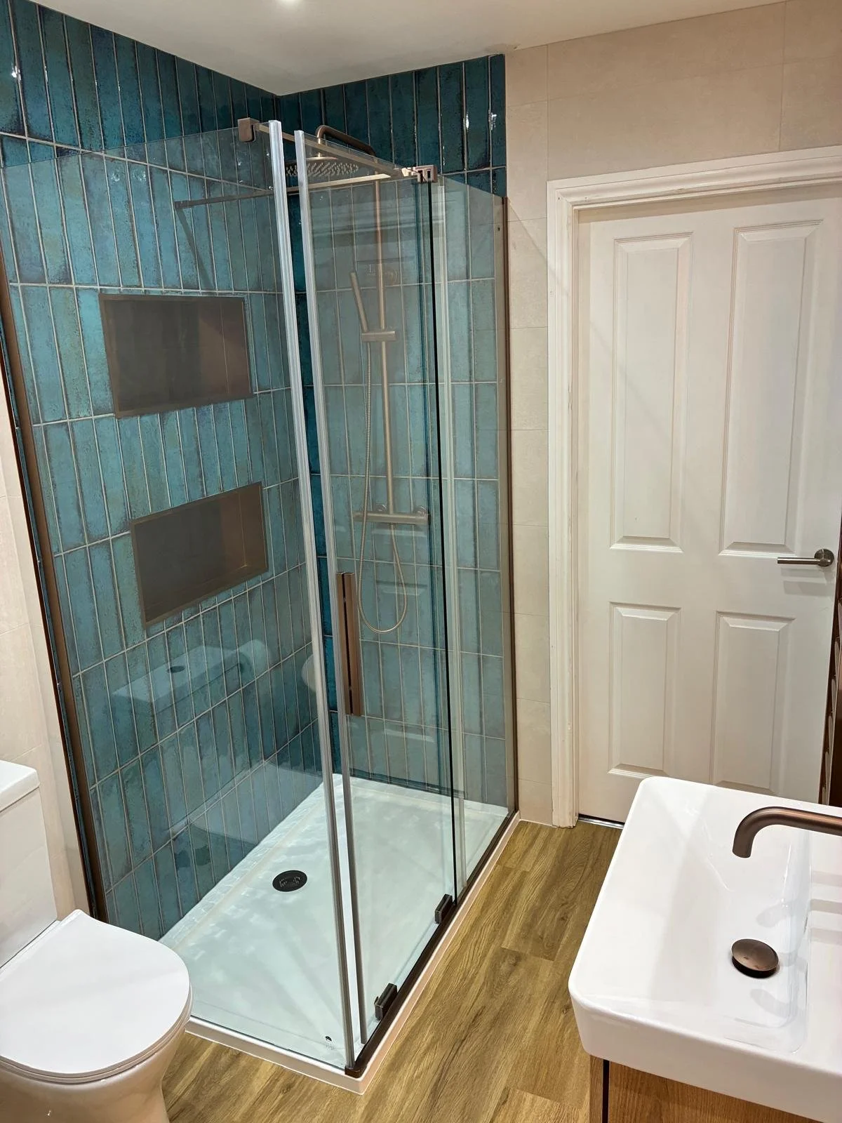 One of our displays featuring white and grey large format marble effect tiles, contemporary bath, brushed brass shower and taps, and contemporary grey and wood effect unit with sit-on sink bowl in a chevron texture..