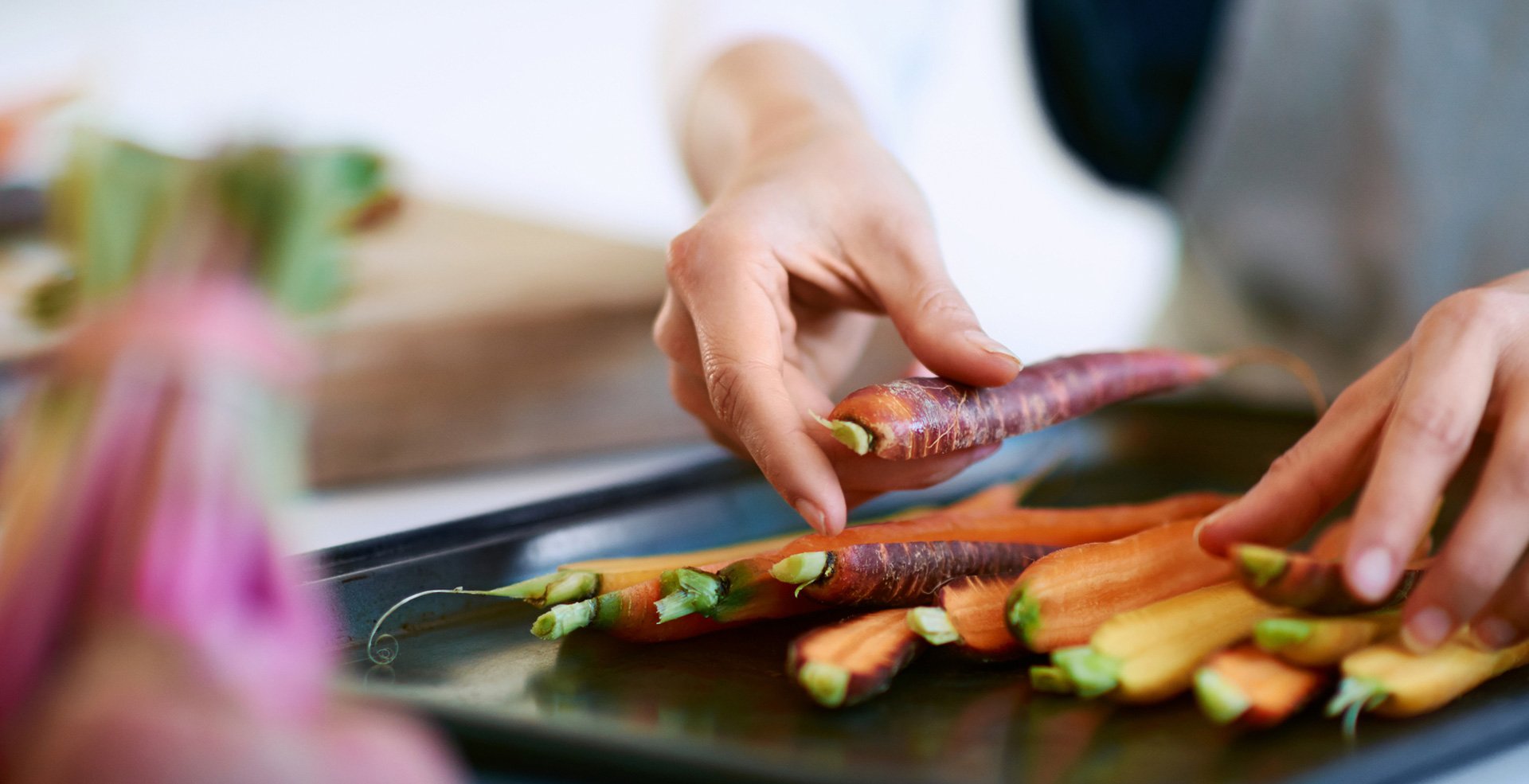 Person arranging multicolored carrots on a baking tray.