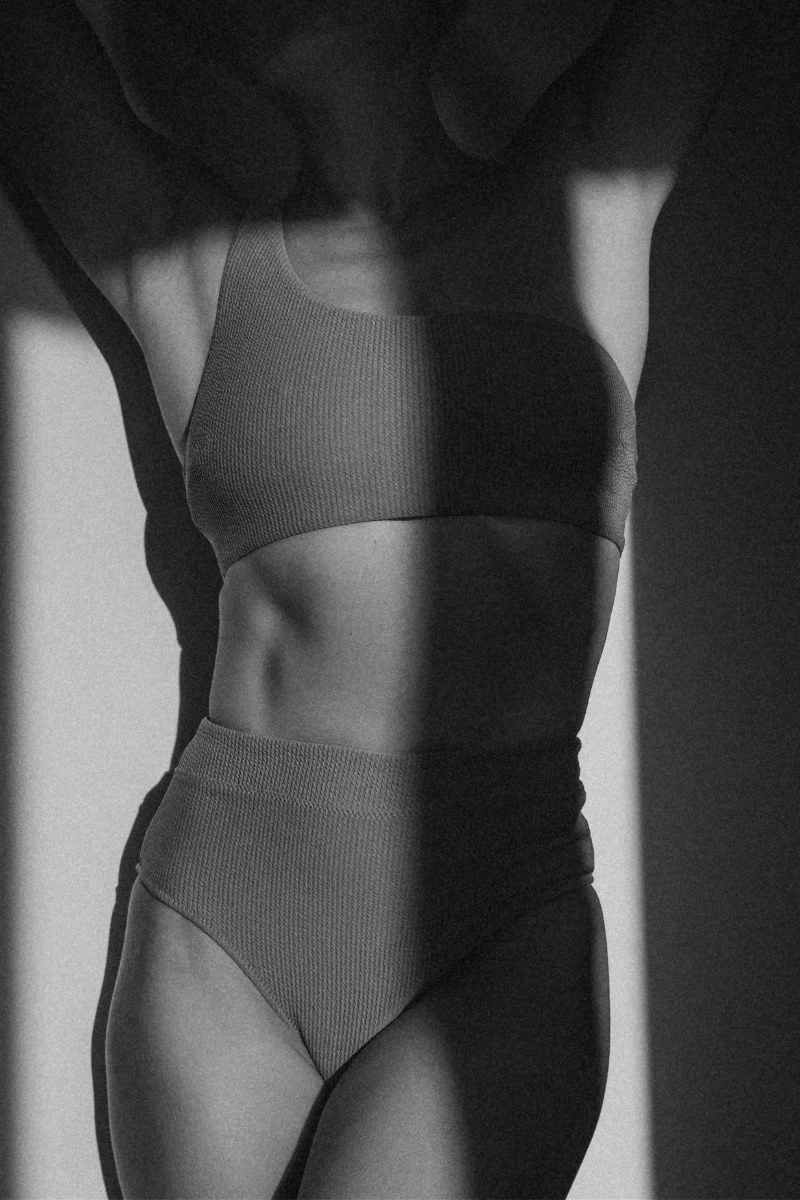 Black and white photo of a woman in activewear showing her midsection, with shadows accentuating her abs and waist.